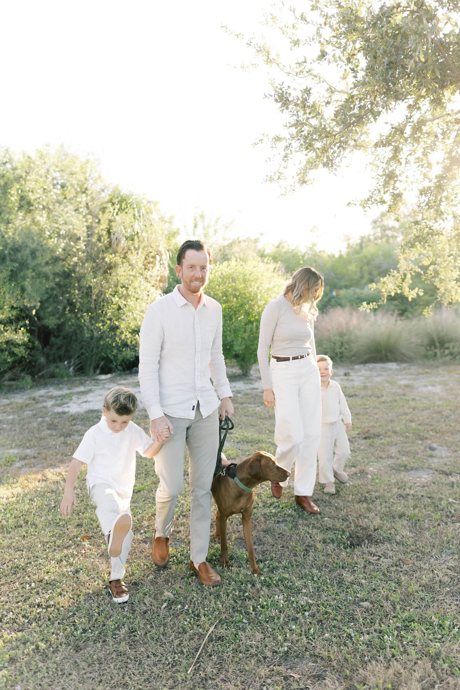 A family and their brown dog enjoying a walk together in a sunlit natural setting.
