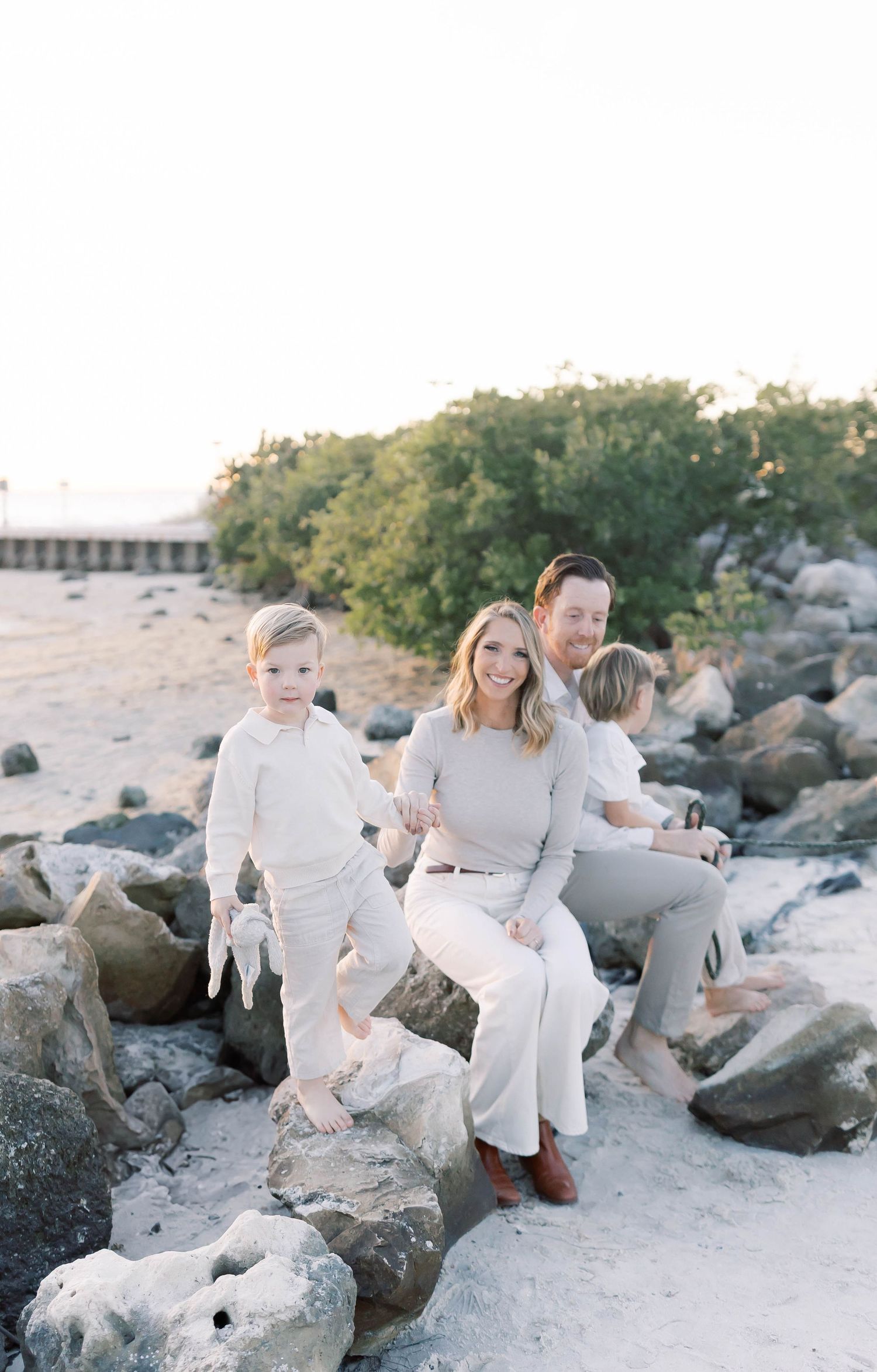 Family enjoys playful moment on rocky beach wearing coordinated white outfits.