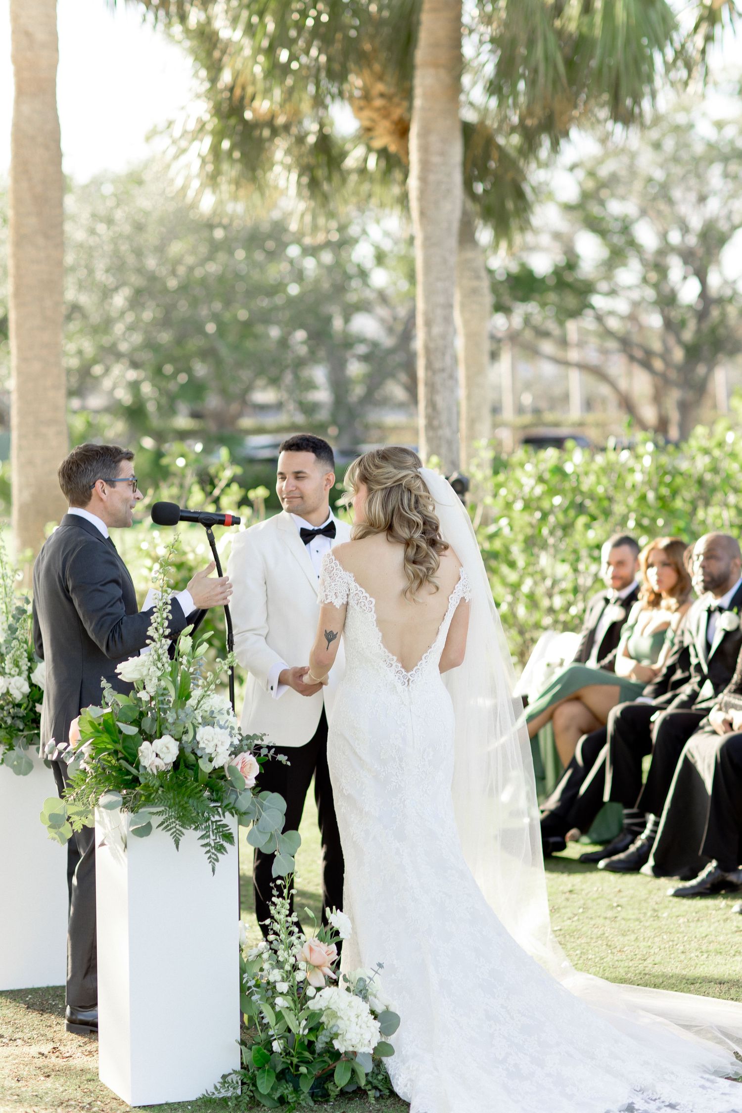 Wedding ceremony setup with white chairs and floral decorations under palm trees.