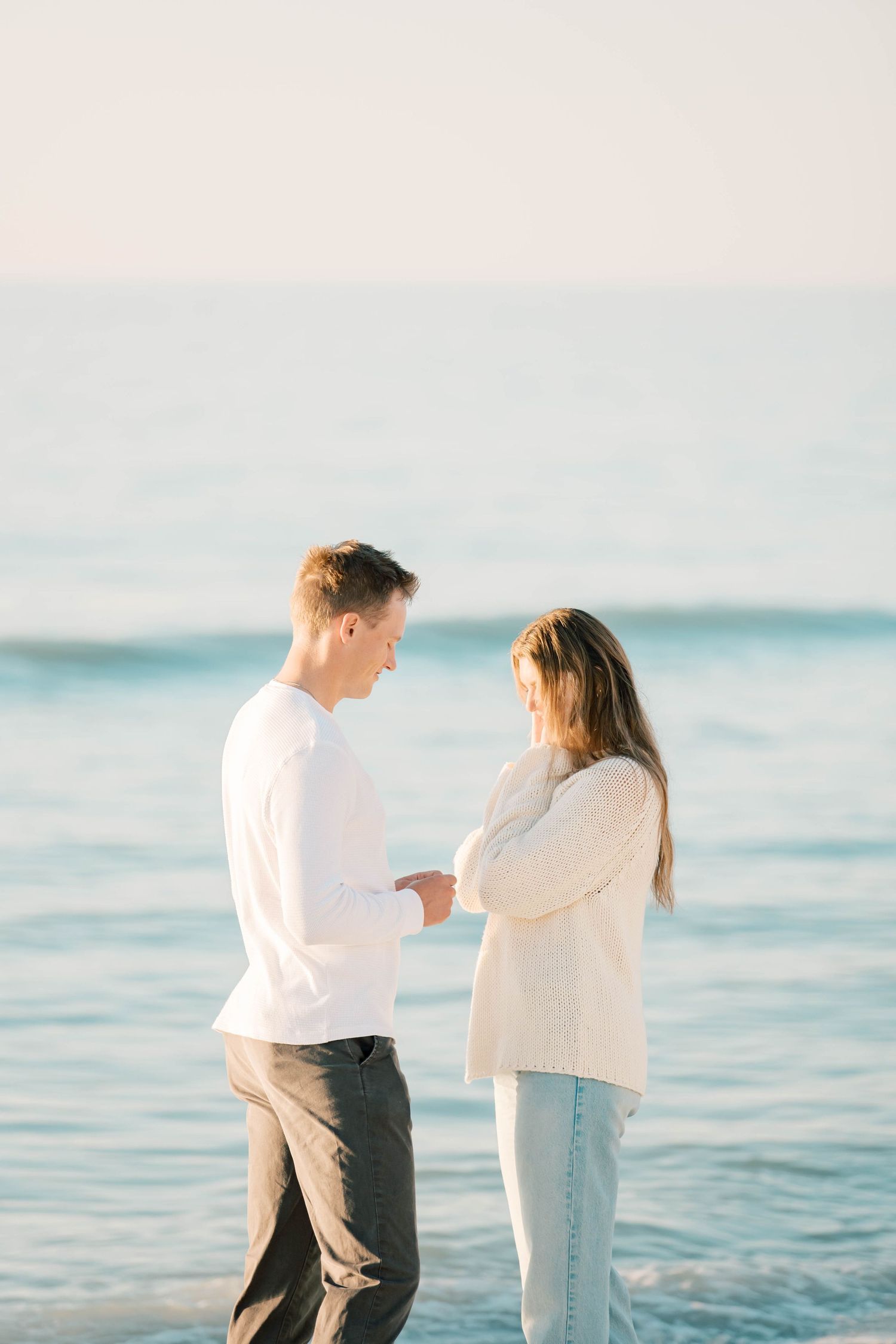 A couple shares an intimate moment while looking at something between them on a beach at sunset.
