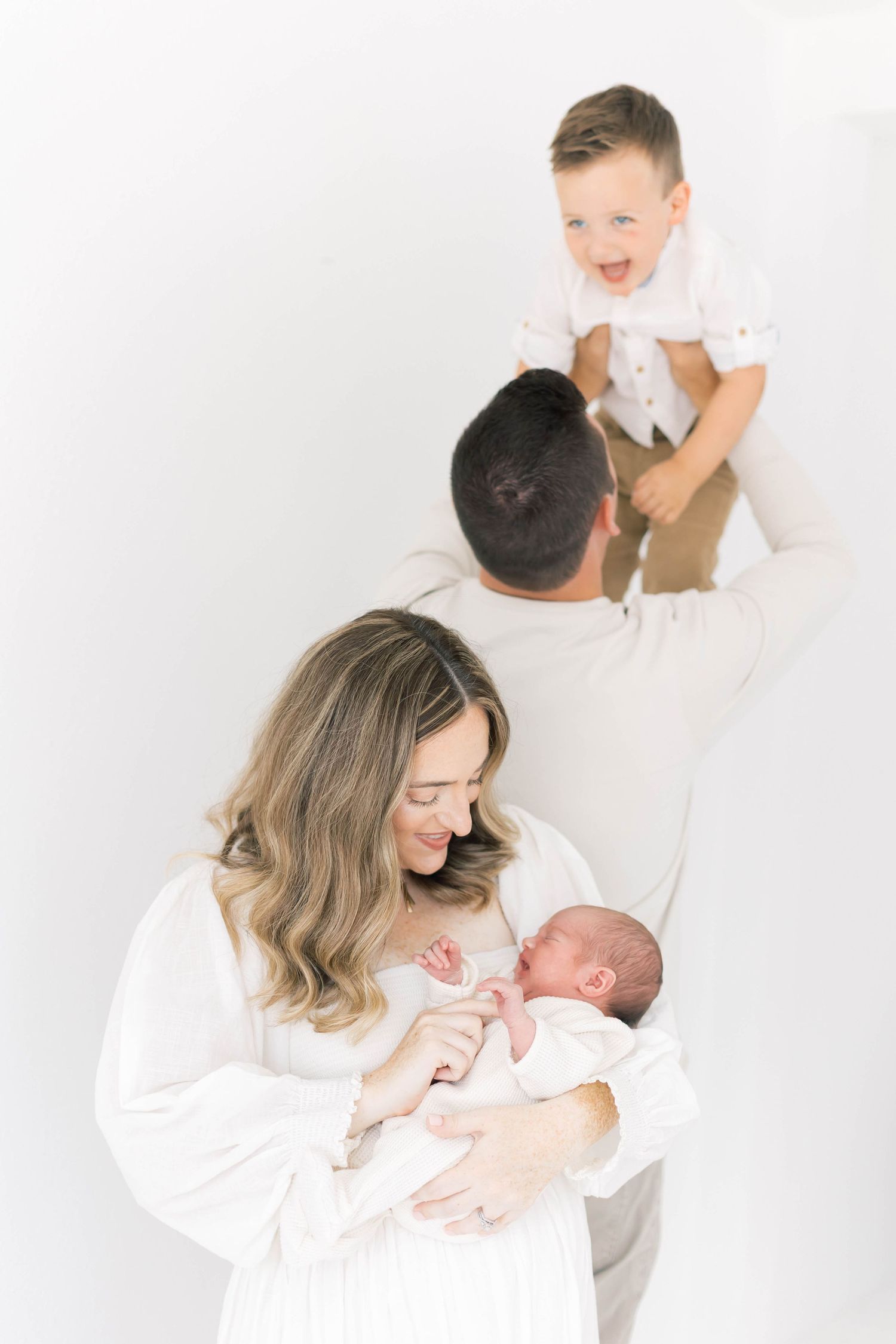 Sweet family interactions with newborn baby in bright white studio setting.