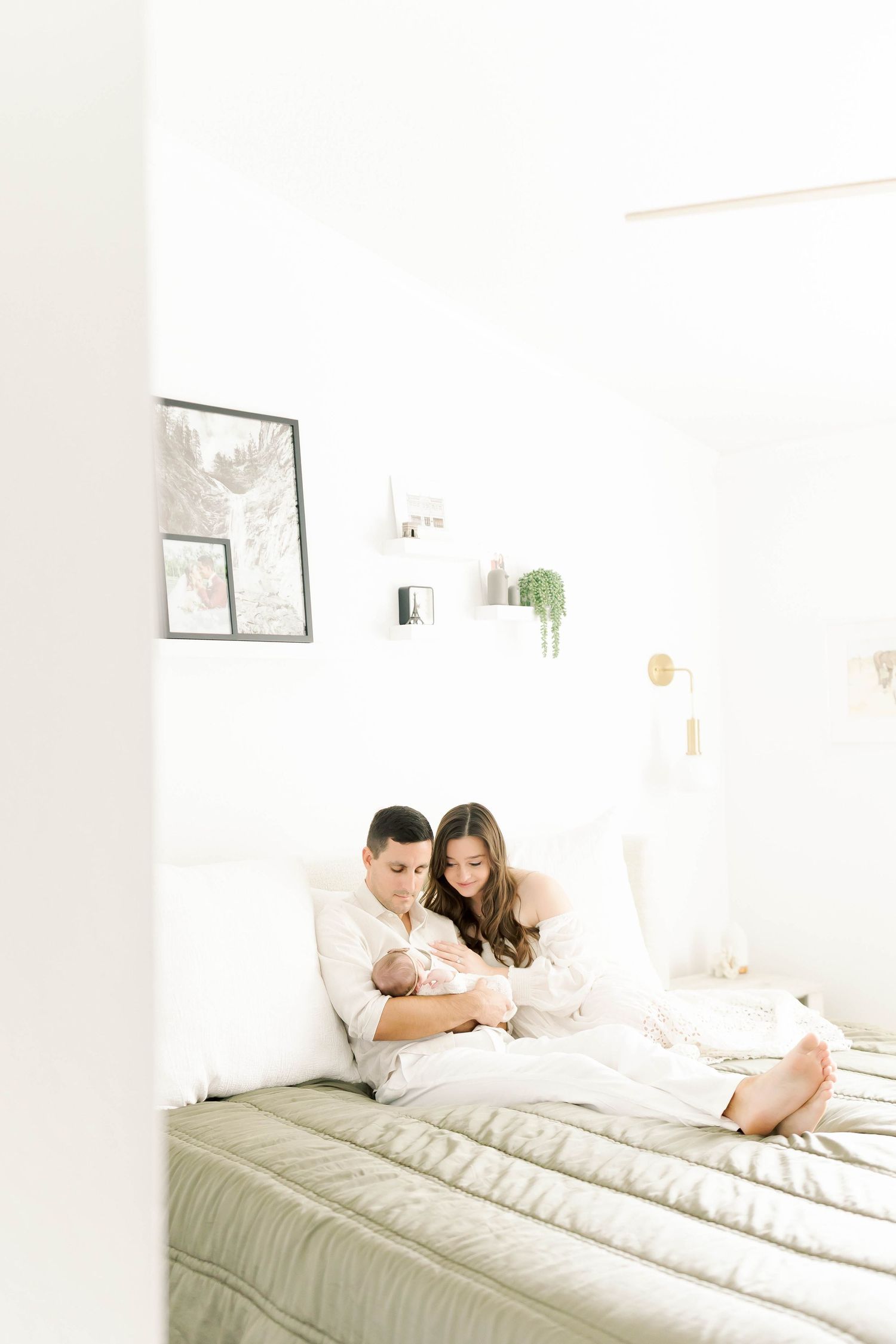 Parents relaxing with newborn baby in minimalist white bedroom with wall art.