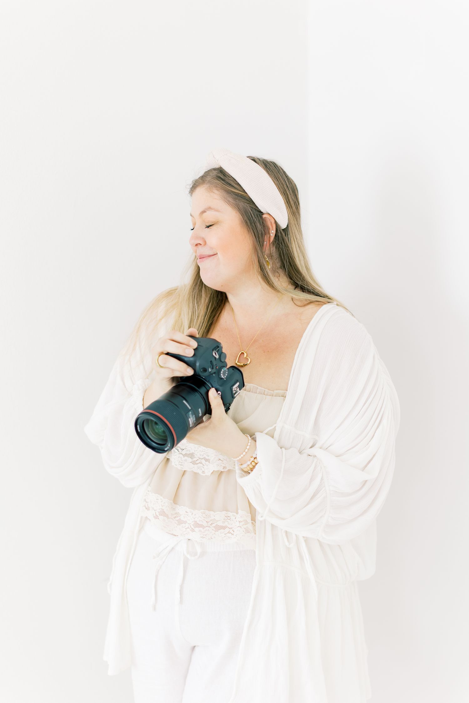 Photographer in white attire holds professional camera against minimalist background.