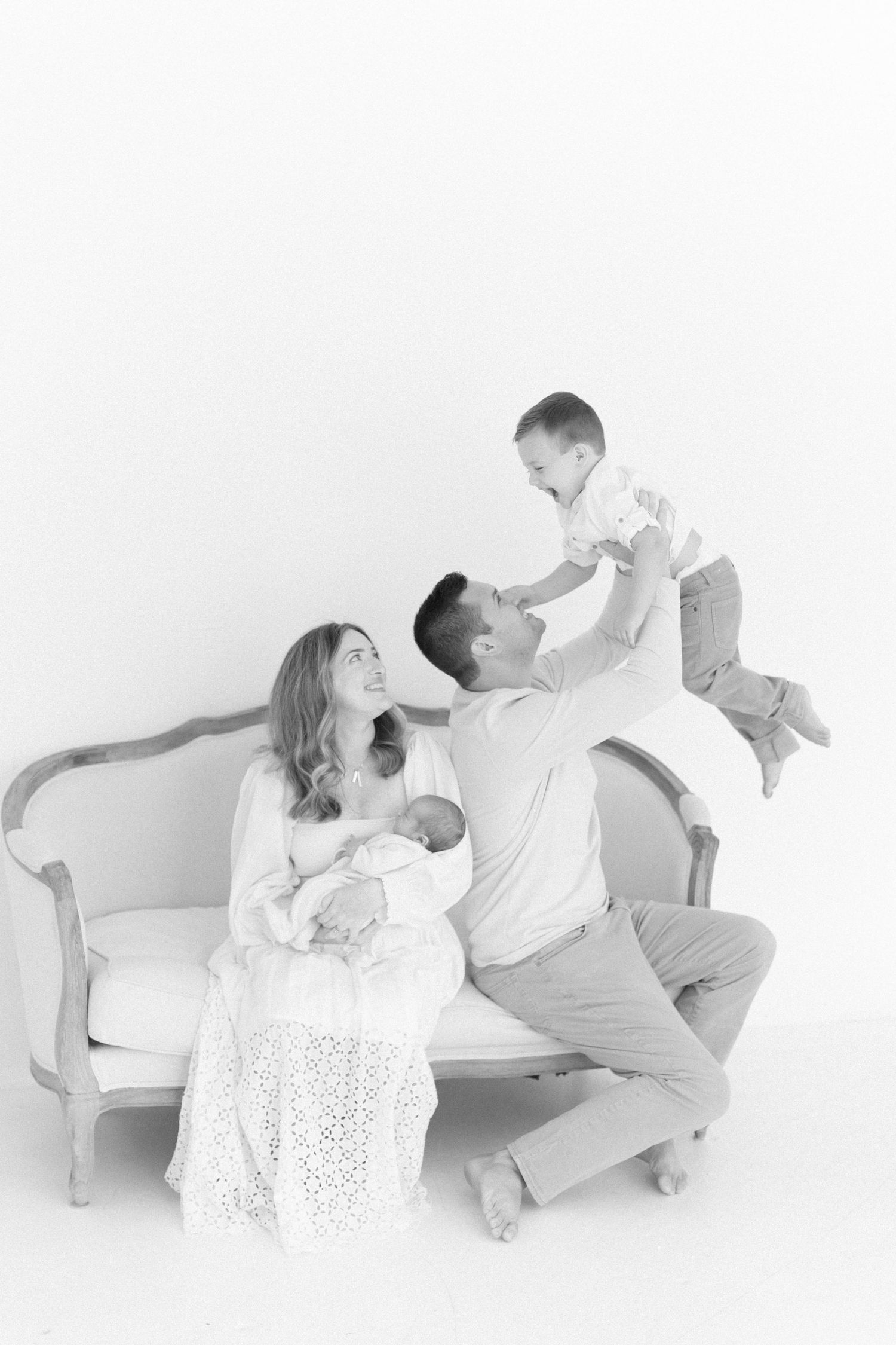 Playful family poses on vintage sofa during minimalist photo session.