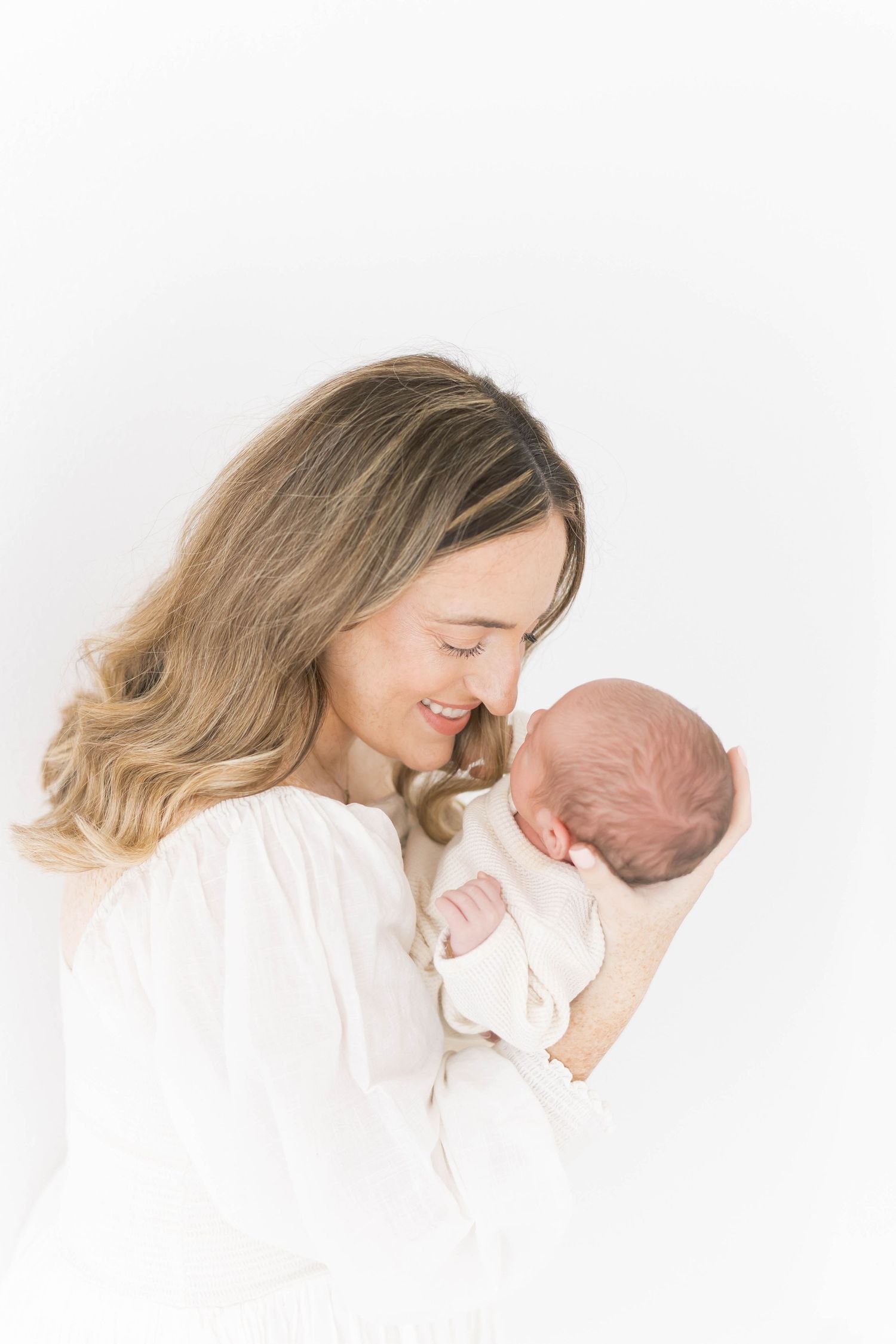 Intimate newborn photography with mother in white against bright background.