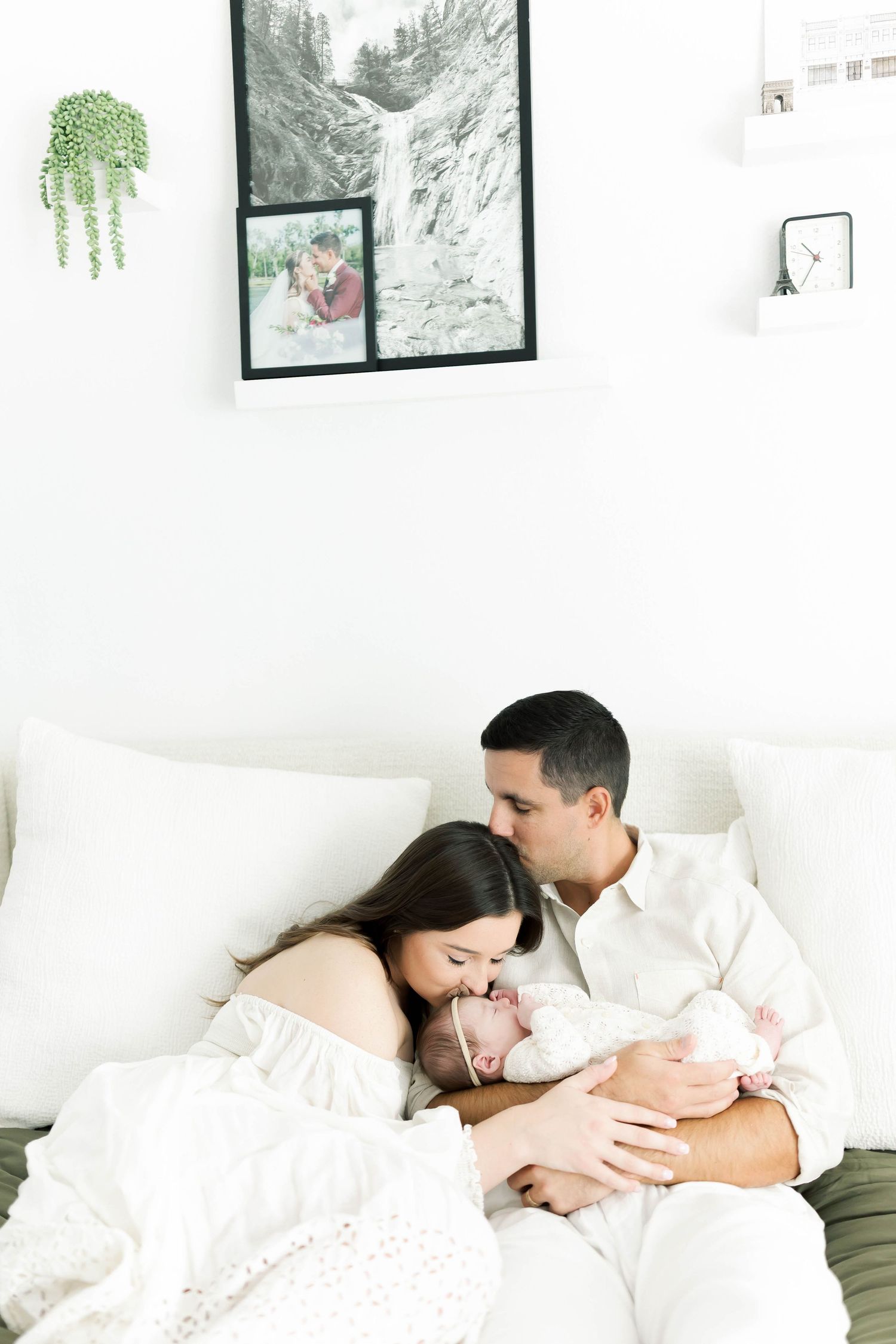 Family resting together on olive green bedding in modern bedroom setting.