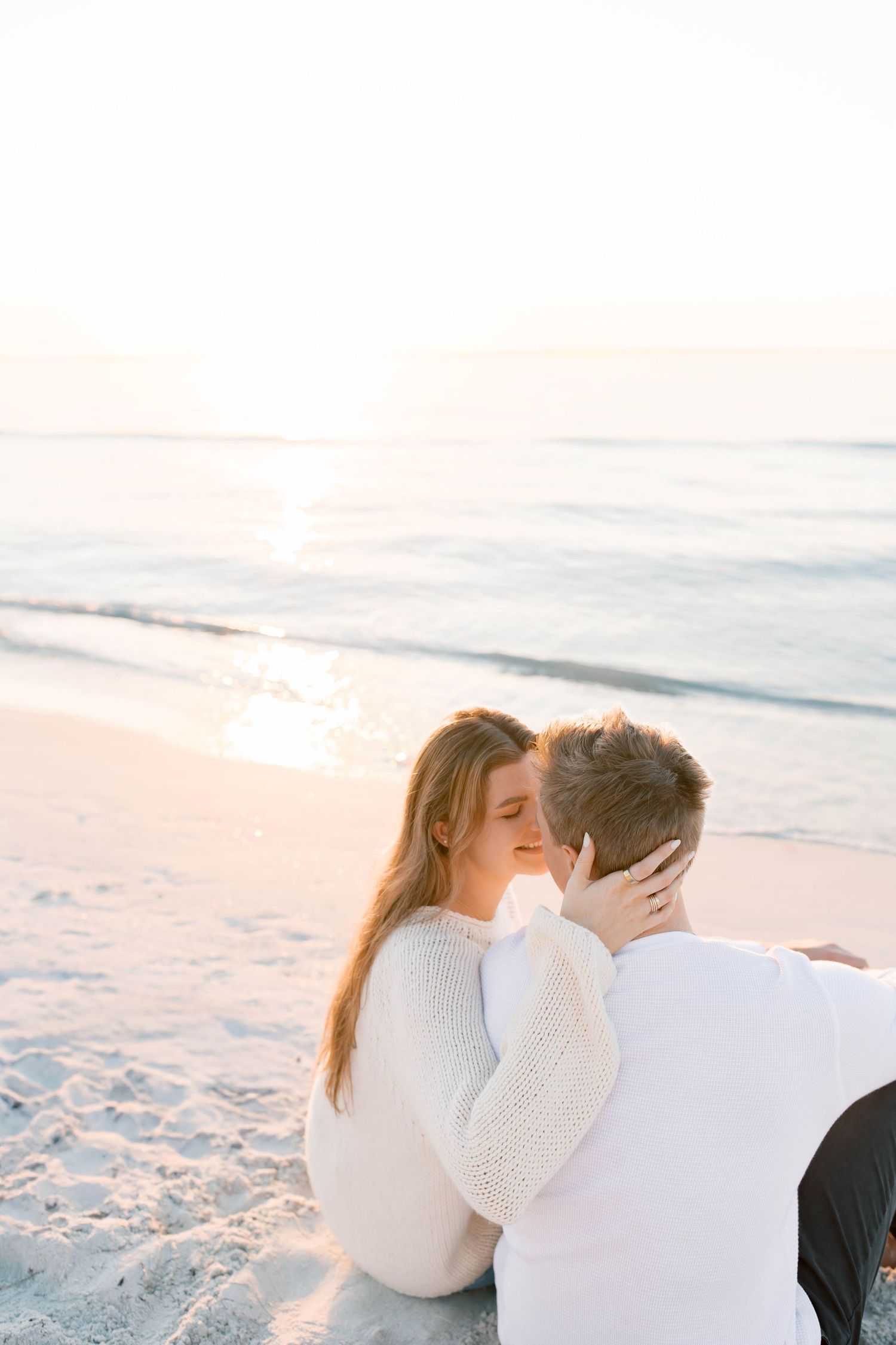 Intimate moment shared between couple on beach wearing white sweaters.