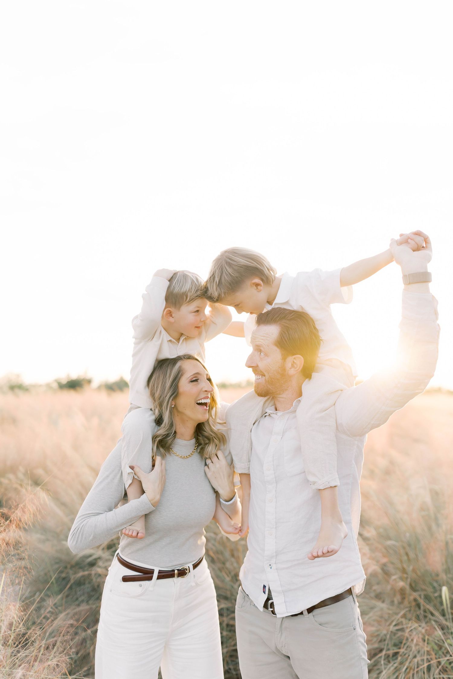 Family laughing and dancing together in a field at sunset.