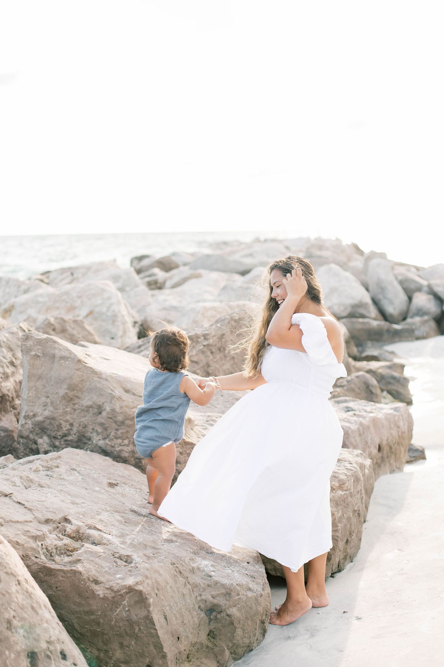 Family exploring rocky beach terrain together in white and blue clothing.