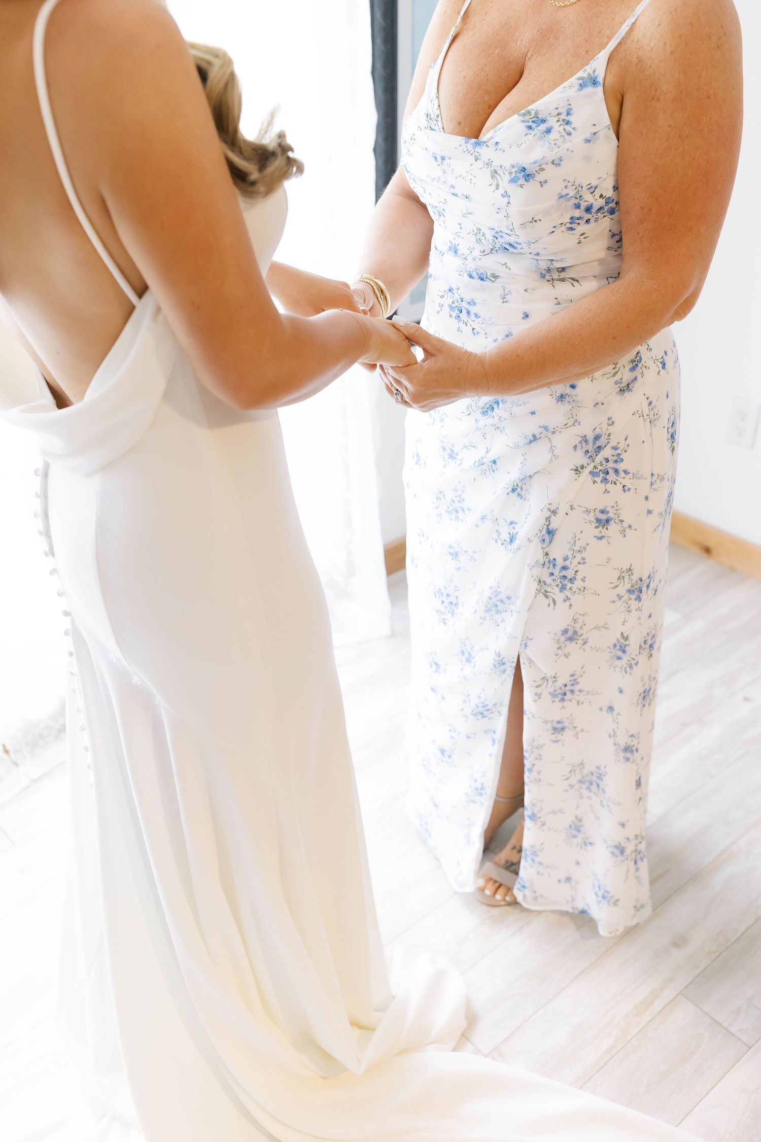 Wedding preparation scene with two people in white and floral dresses embracing.
