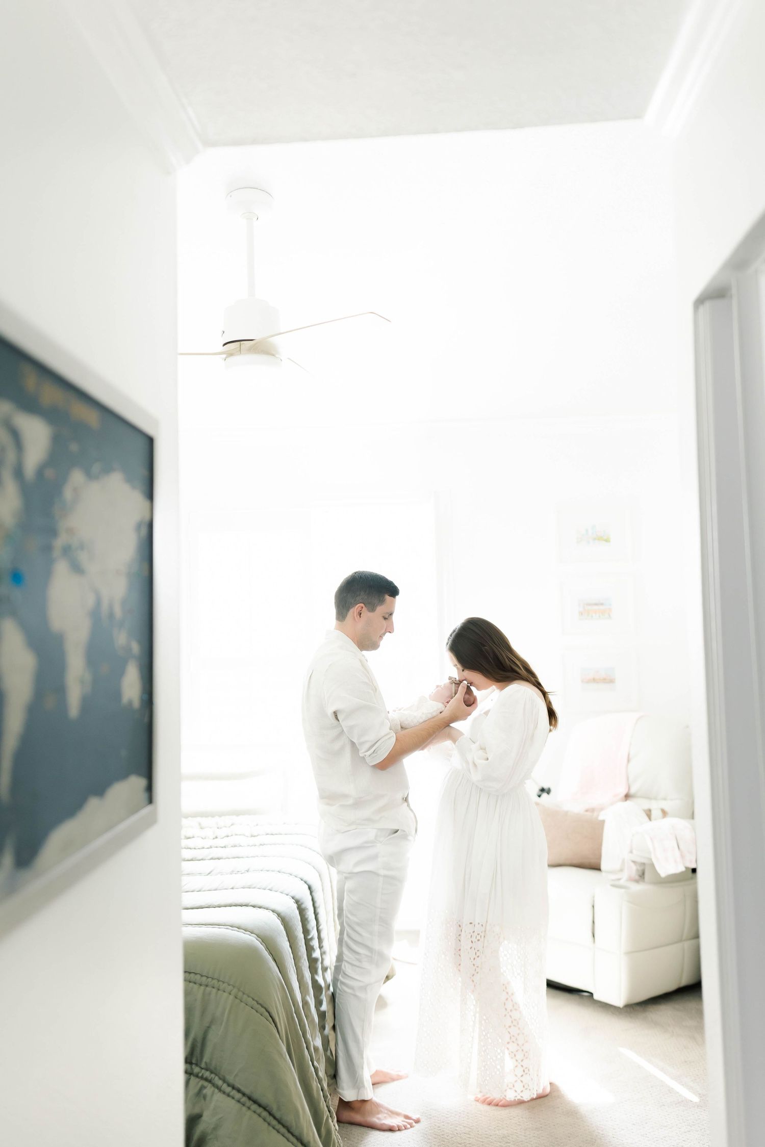 Parents in white clothing share intimate moment with baby in modern bedroom.