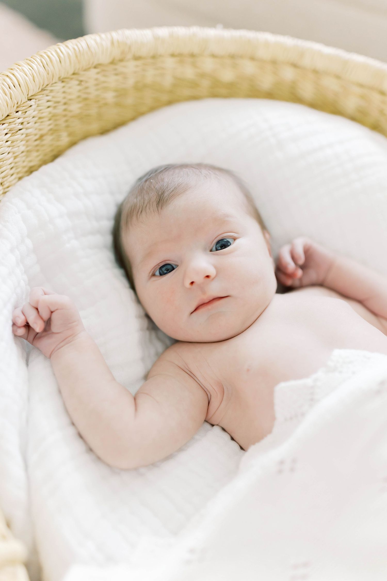 Adorable baby lying in cozy white bedding with bright eyes looking at camera.