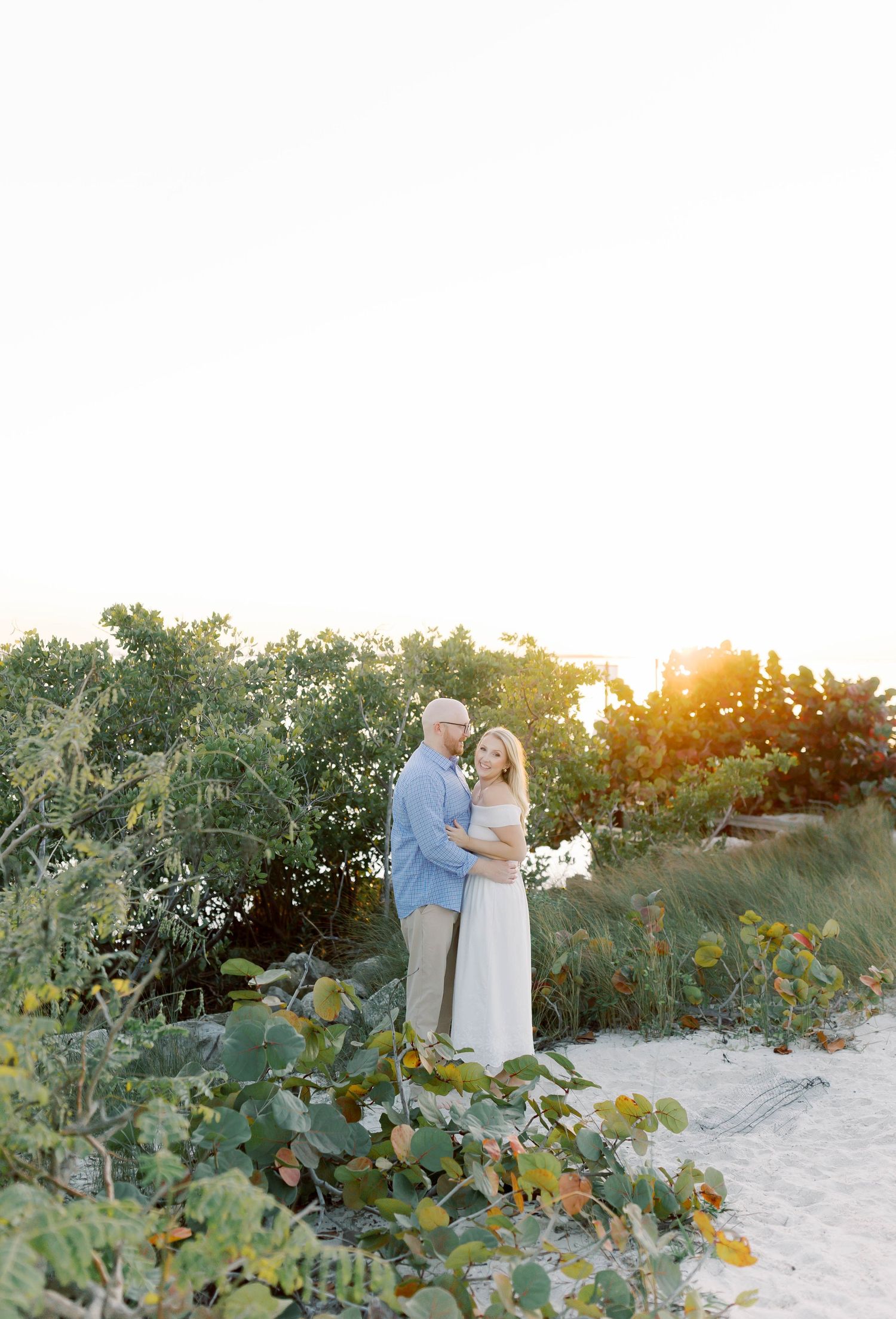Sunset beach photoshoot with couple among coastal vegetation.