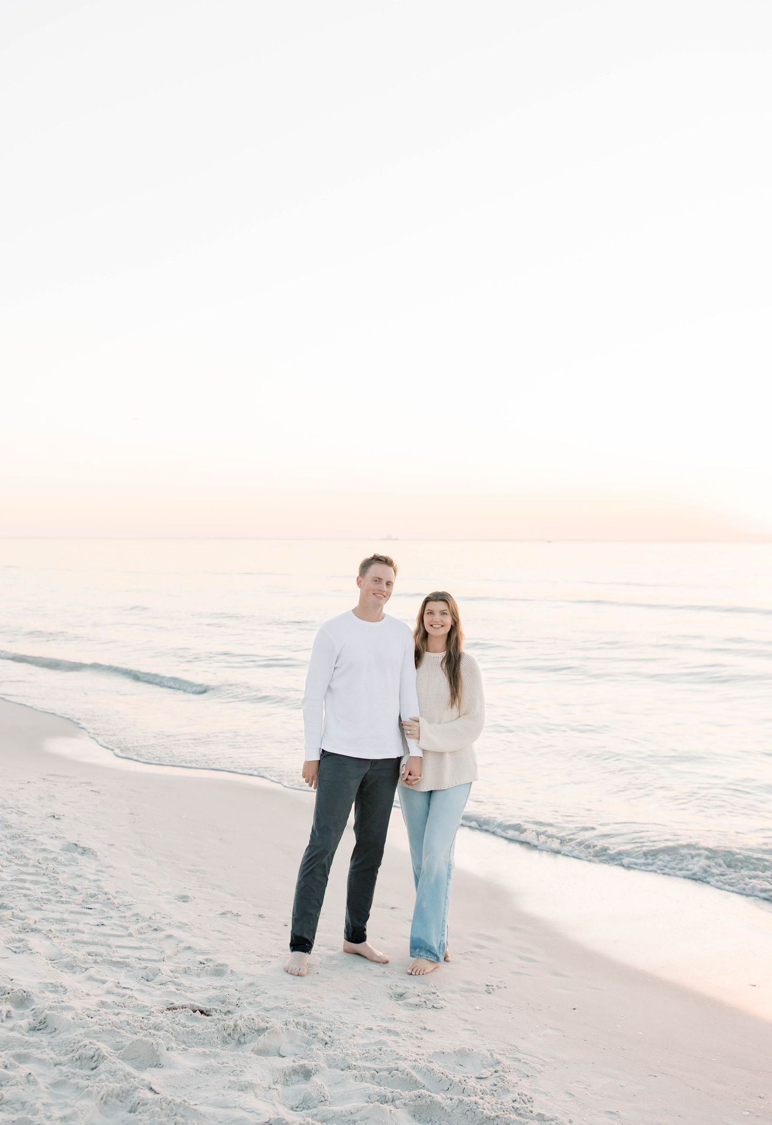 Couple walking along shoreline at sunset in casual beach attire.