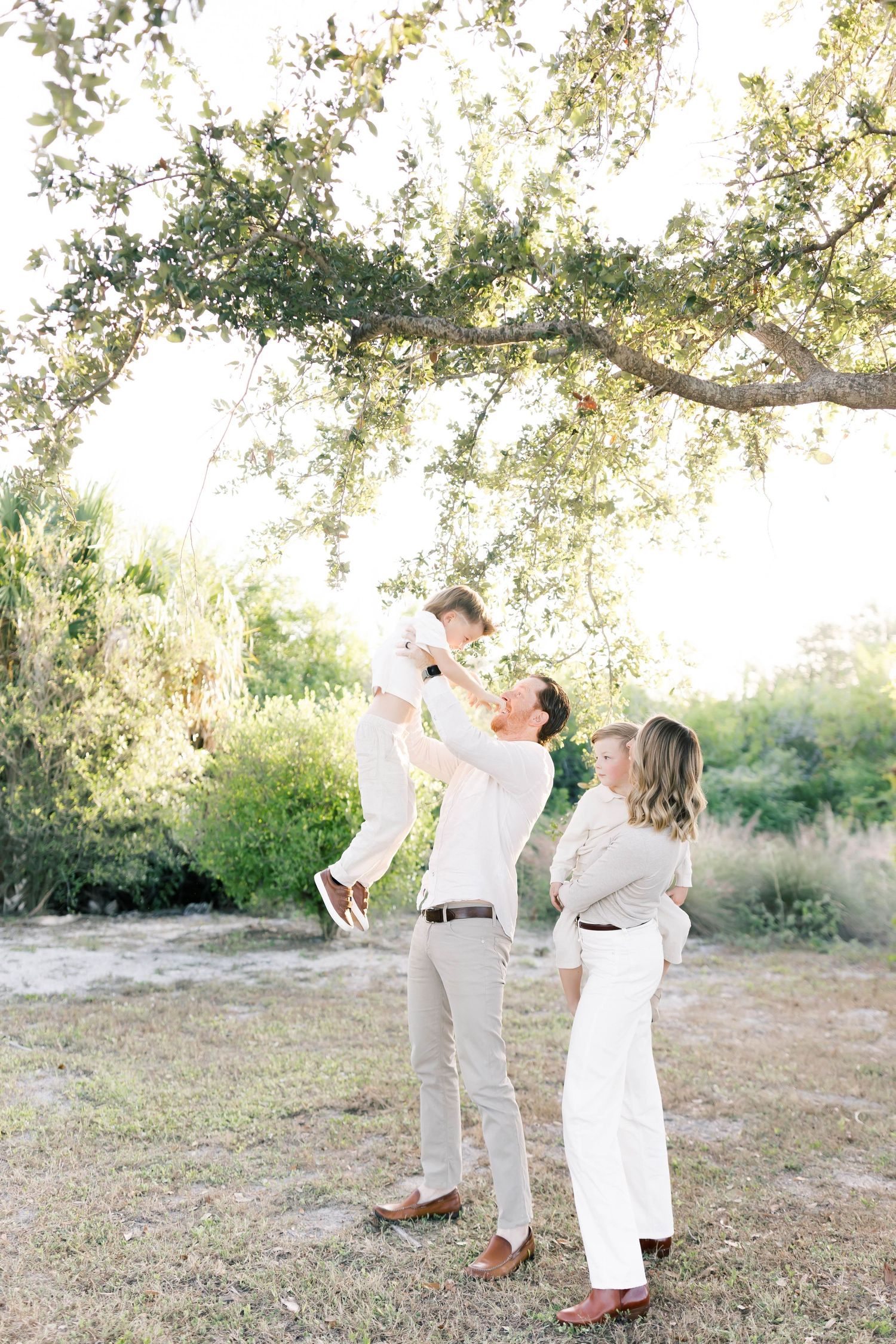 A joyful family moment with lifting and playing under a beautiful tree canopy.
