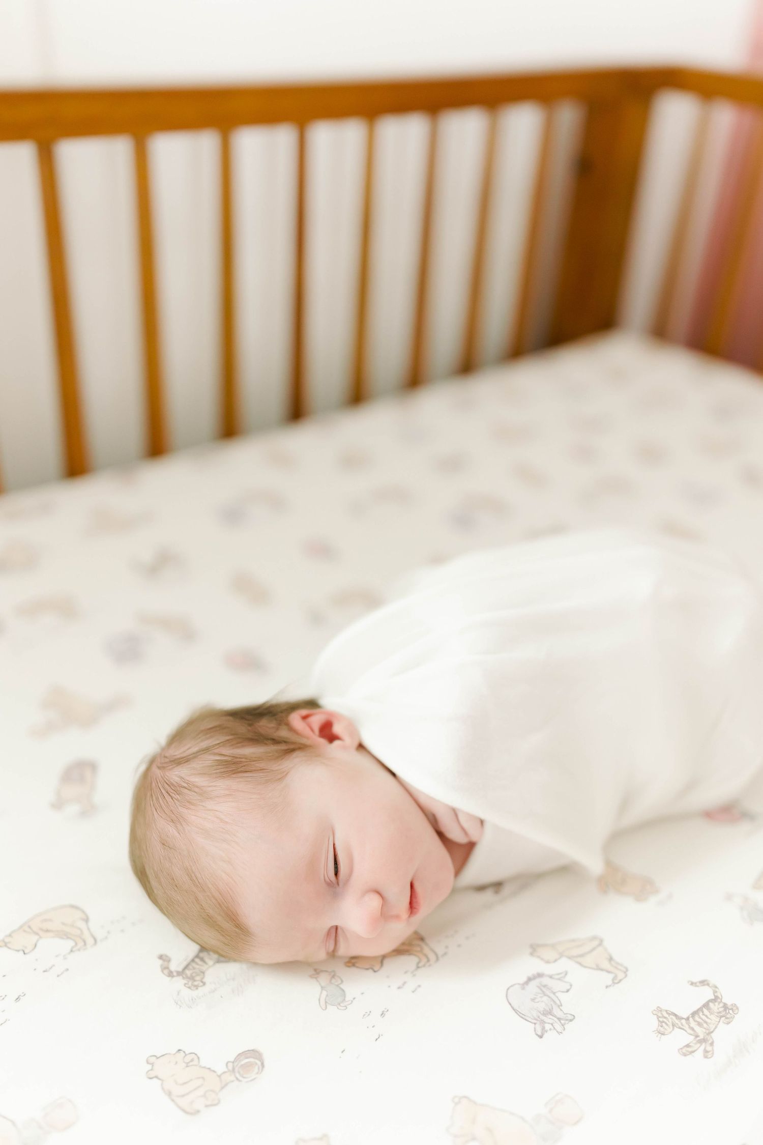 A sleeping newborn baby lies peacefully on patterned crib sheets in a wooden crib.