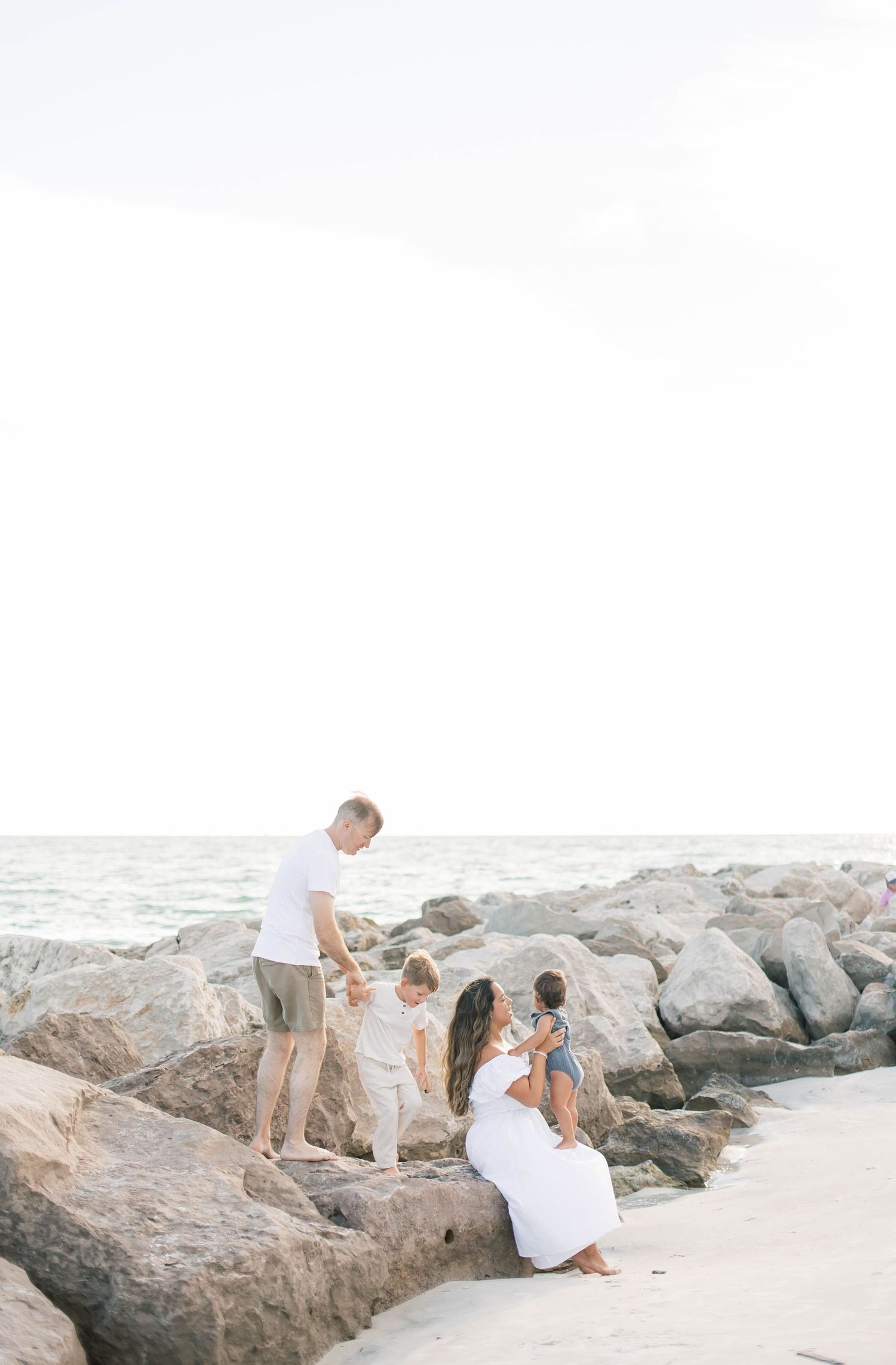 A family plays together on a beach with large rocks during a bright sunny day.