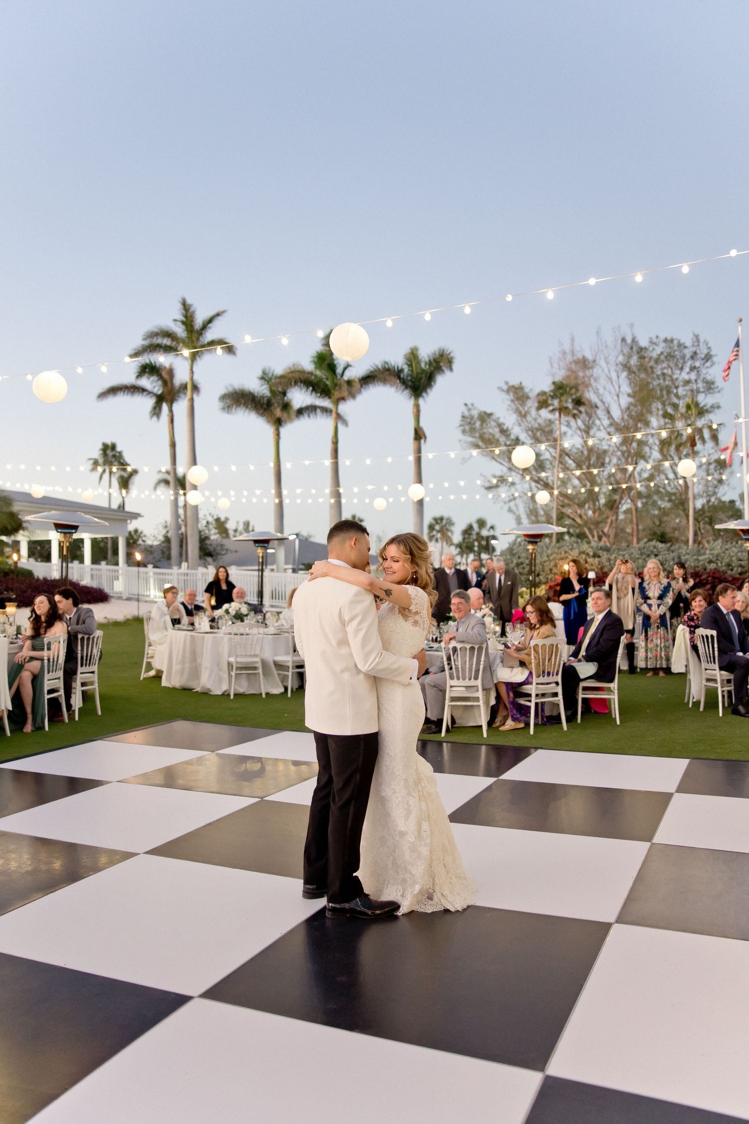 Couple sharing their first dance on a black and white checkered dance floor at an outdoor wedding reception.