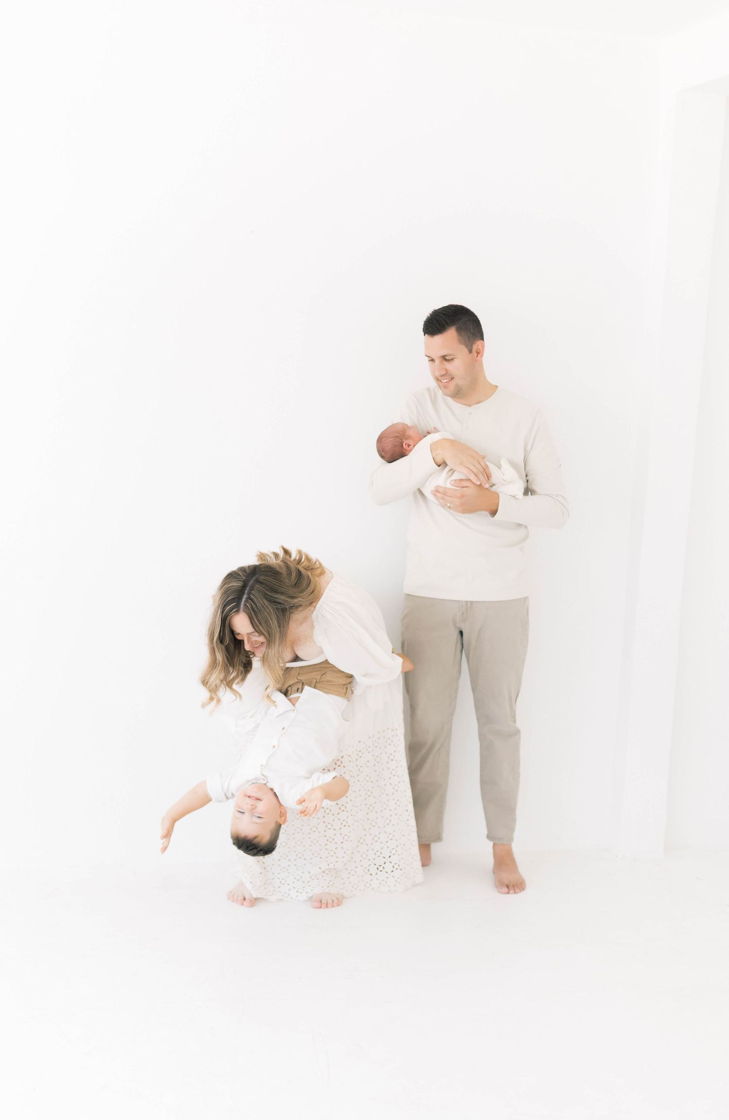 Modern family photography with parents and baby in minimalist white studio.