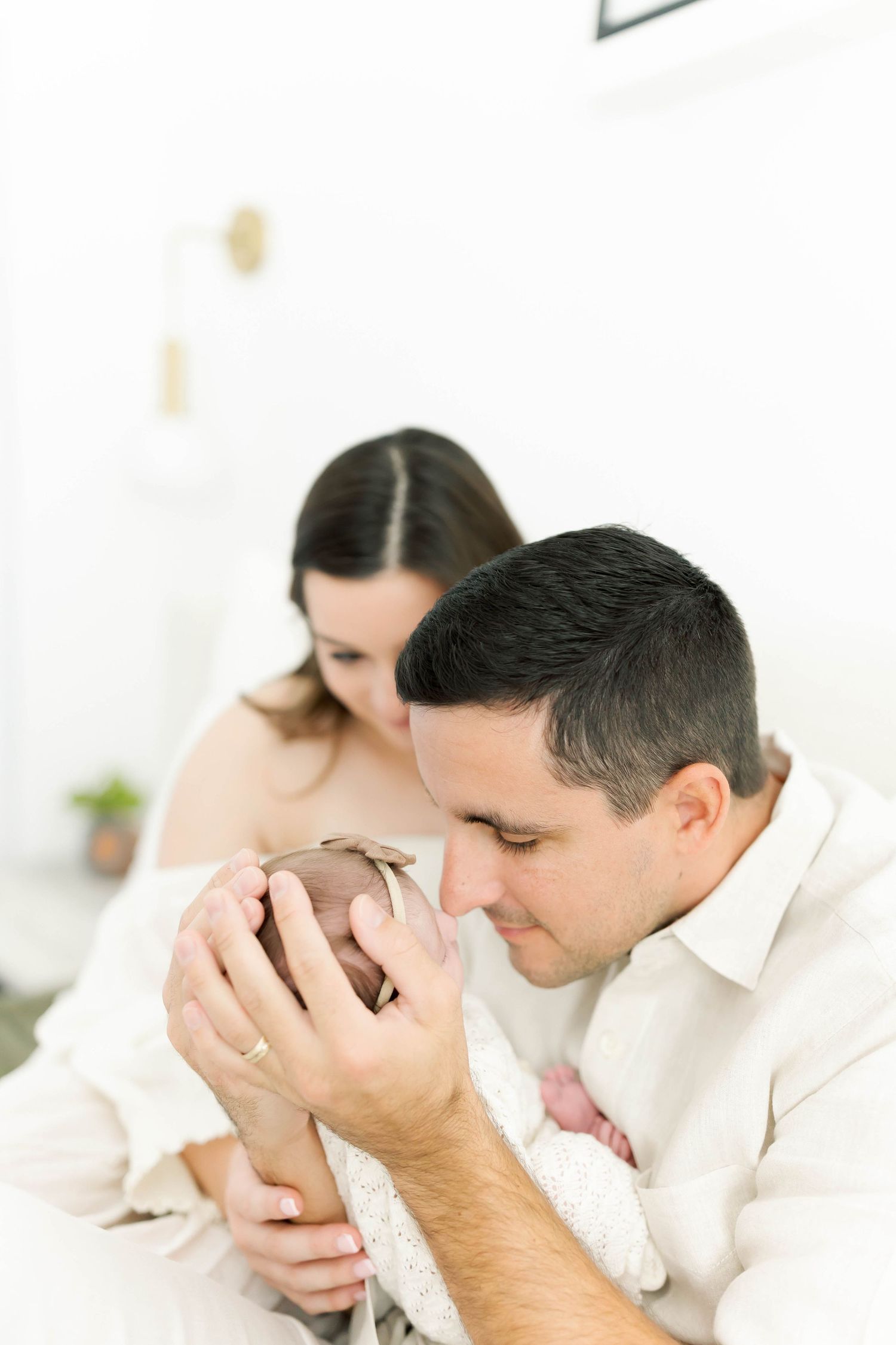 Parents share an intimate moment with their newborn baby in a bright white room.