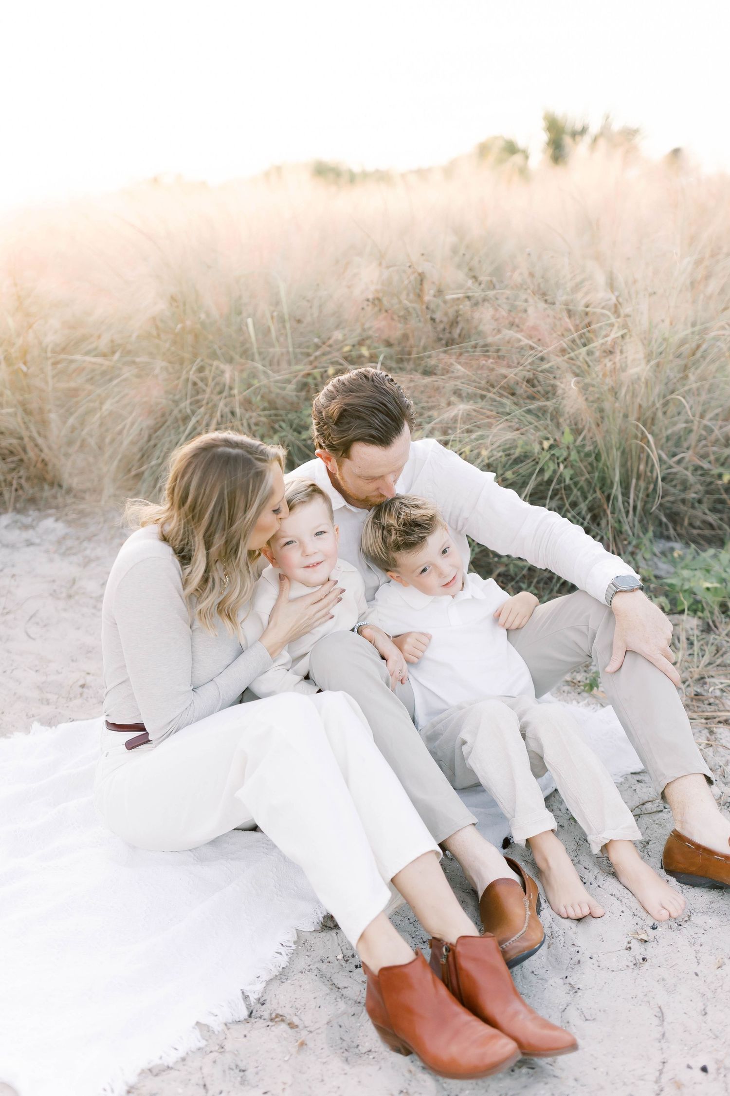 Family relaxing together on sandy ground wearing coordinated white and neutral outfits.