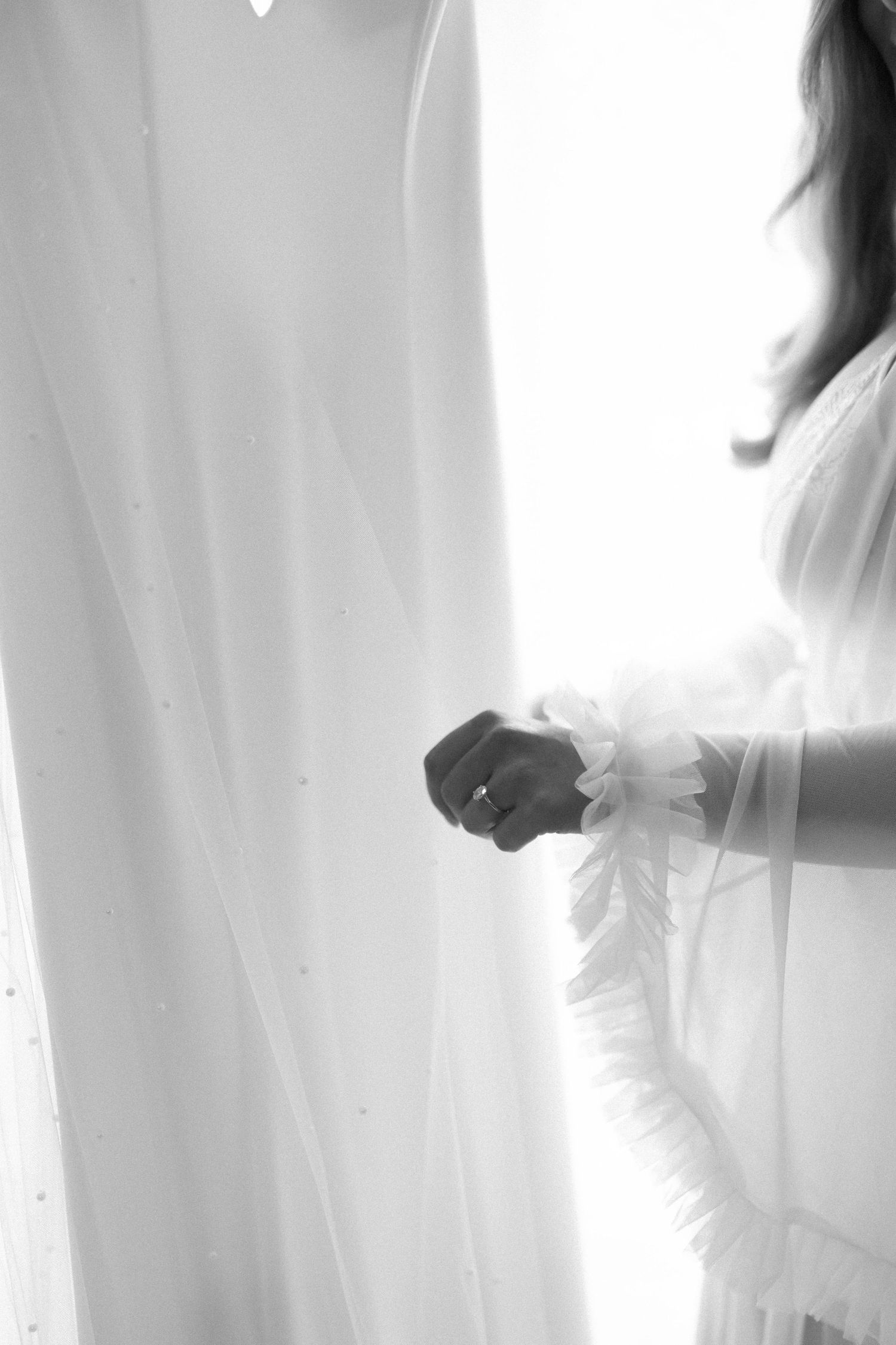 Ethereal silhouette of bride getting ready in white against window light.
