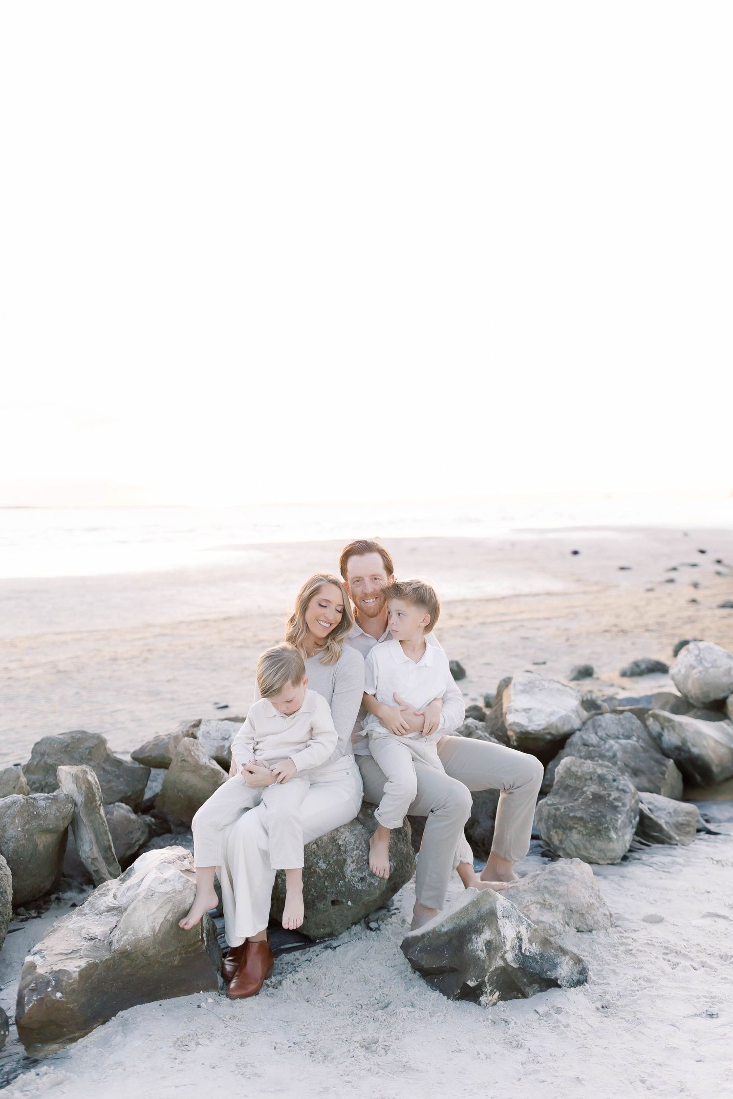 Group relaxes on coastal rocks wearing coordinated white outfits at the beach.