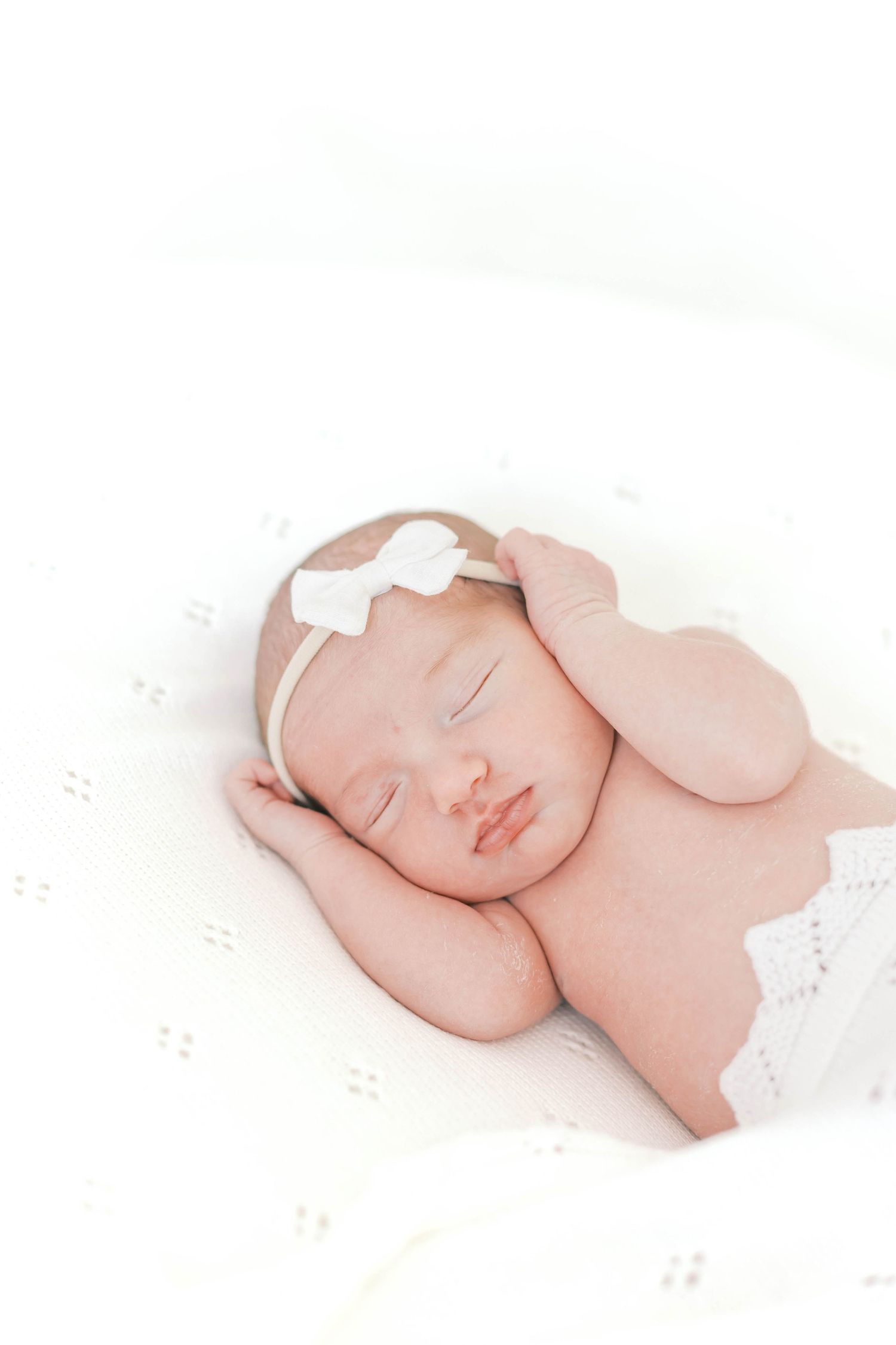 Peaceful sleeping newborn wrapped in white fabric against light background.