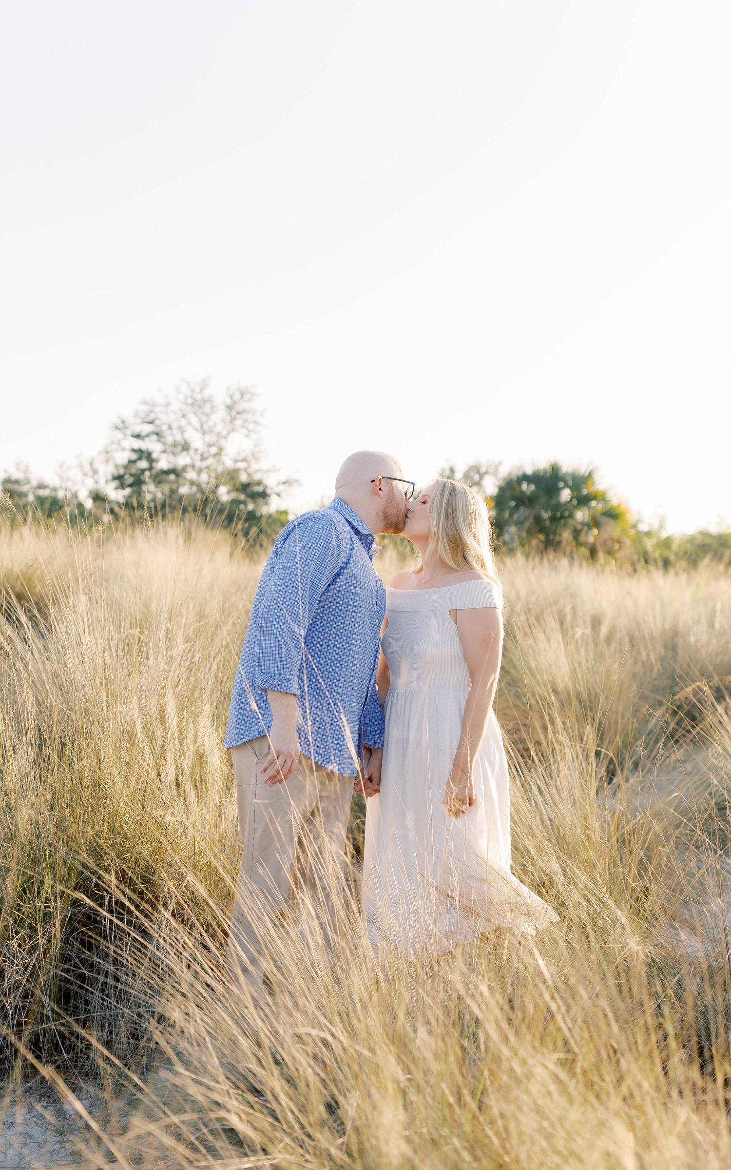 Intimate moment between couple standing in tall grass during sunset.