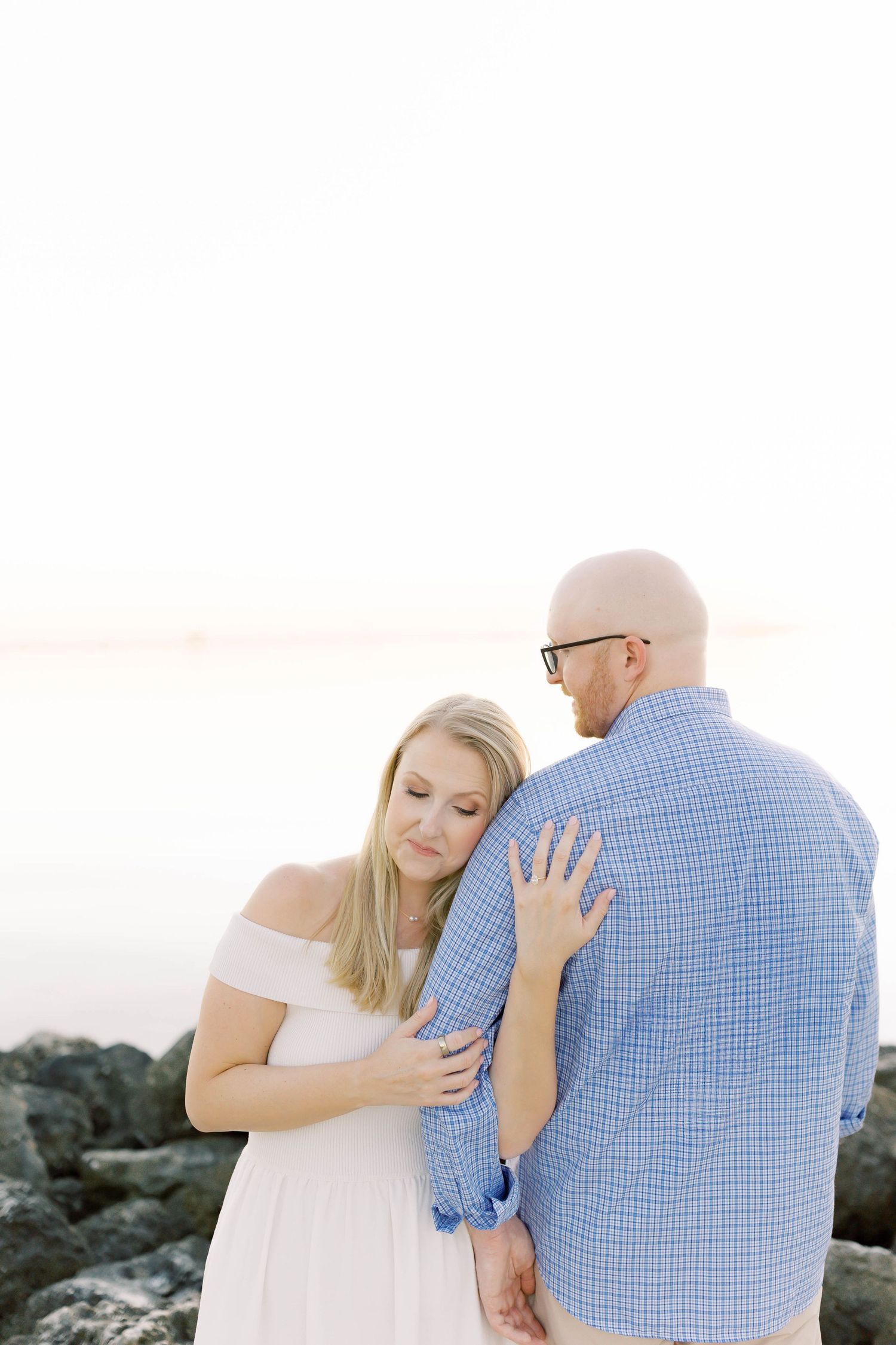 An intimate moment between a couple as they embrace on rocky coastal terrain at sunset.