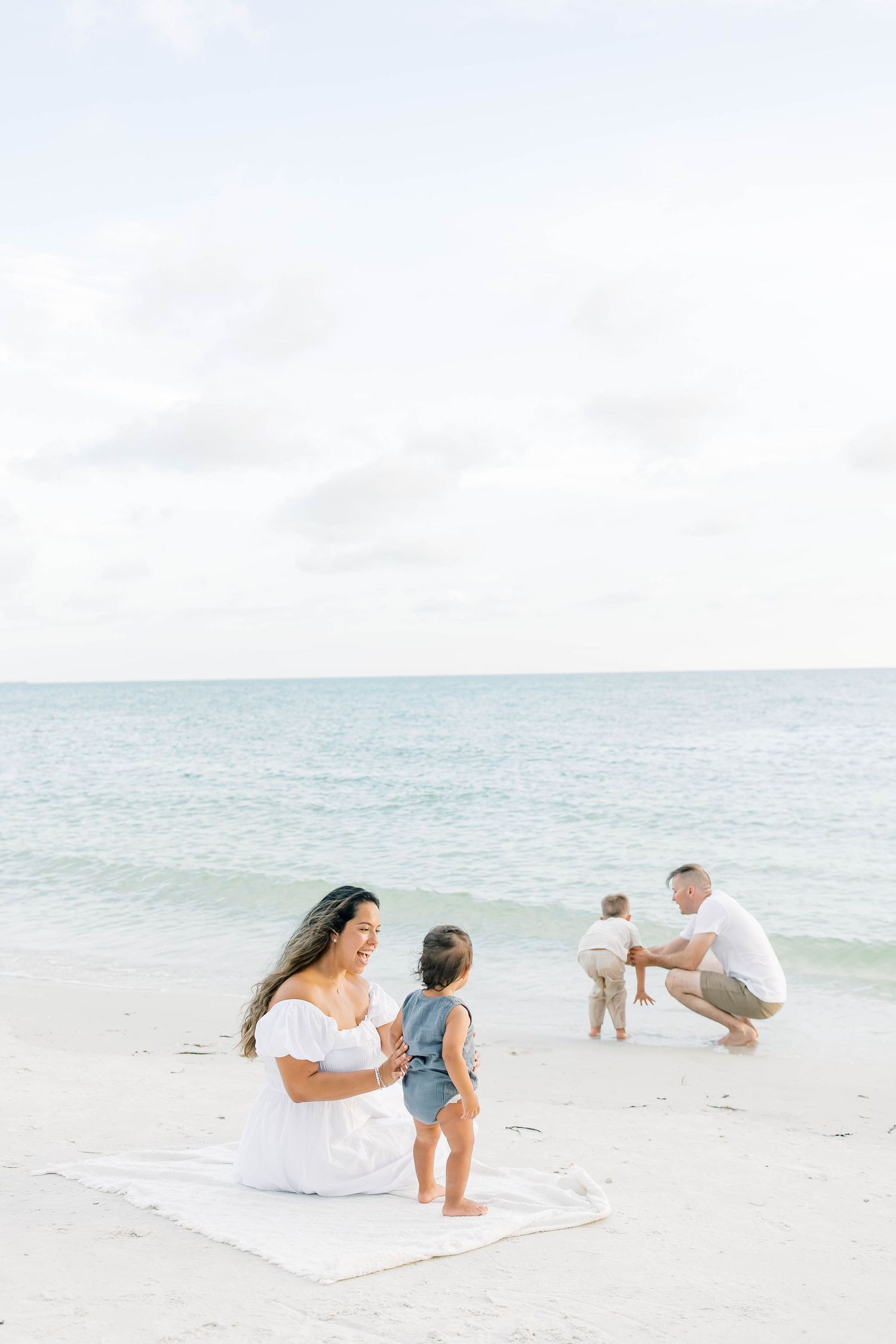 Family enjoying a playful moment together on a bright sunny beach with calm waters.