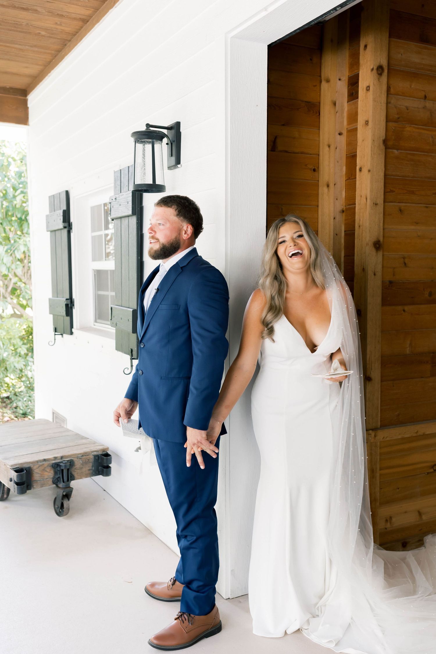 A couple shares a playful first look moment around a corner at their wedding venue.
