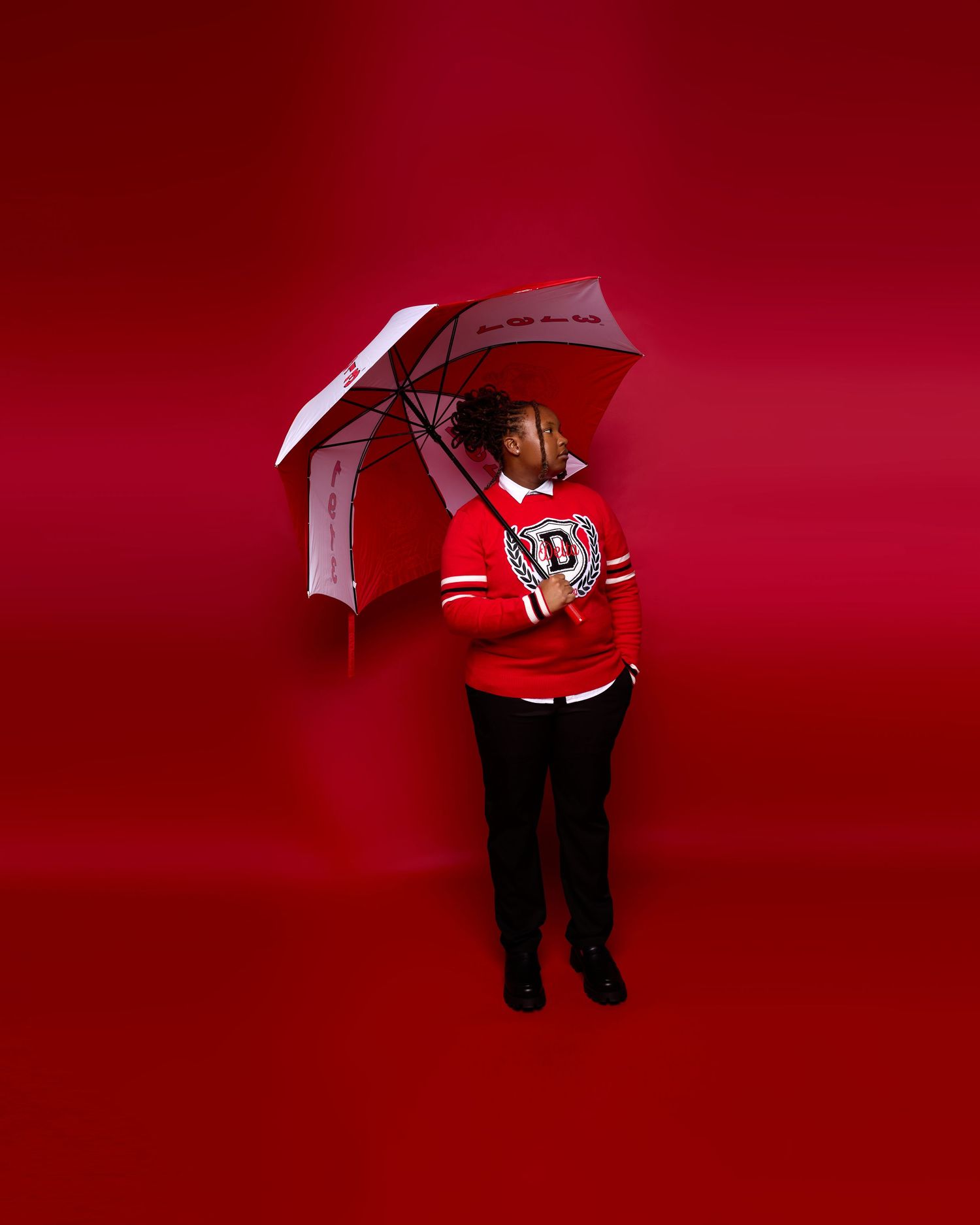 Figure with umbrella poses against vibrant red studio background.