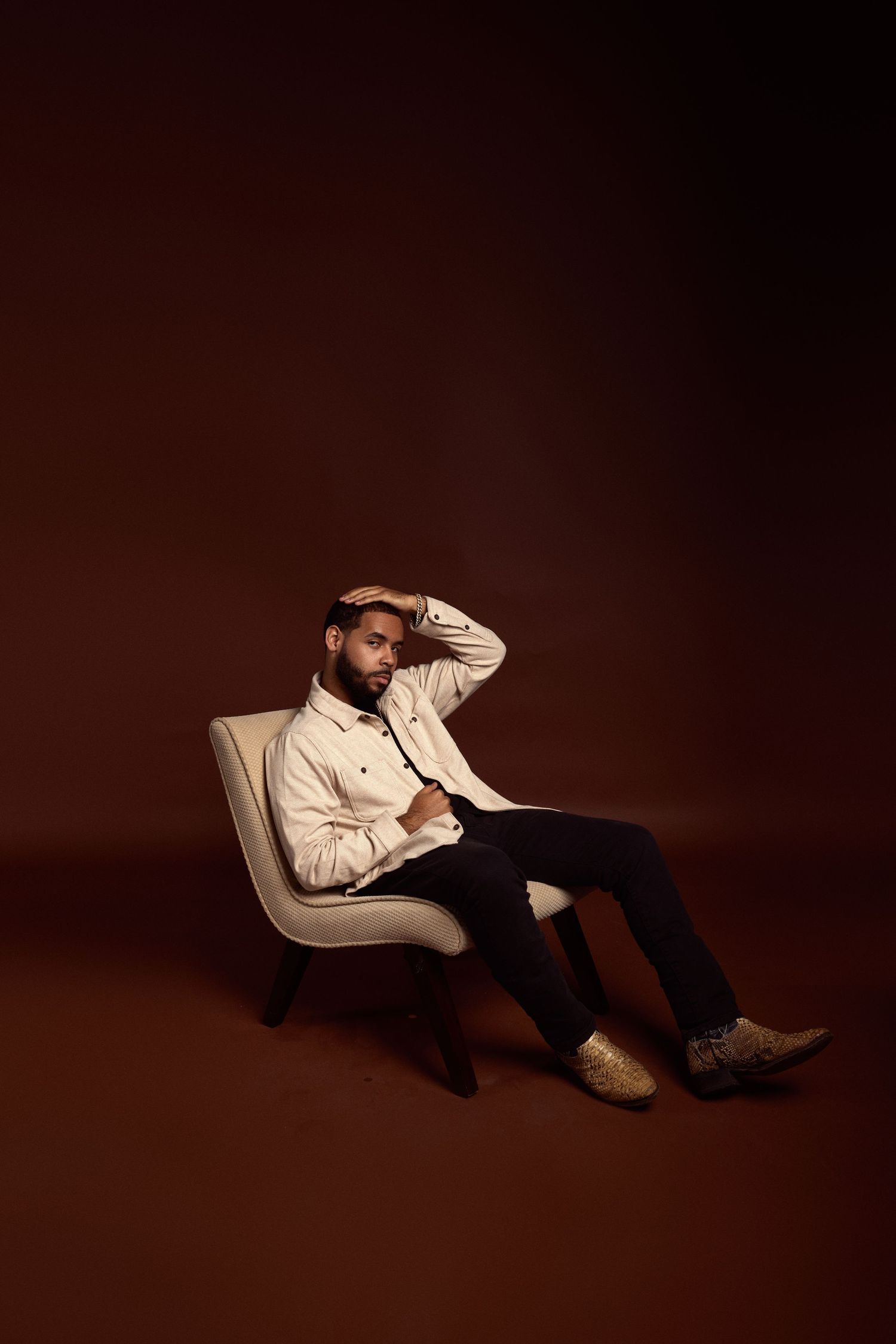 Artistic portrait in cream colored suit against dark background with dramatic lighting.