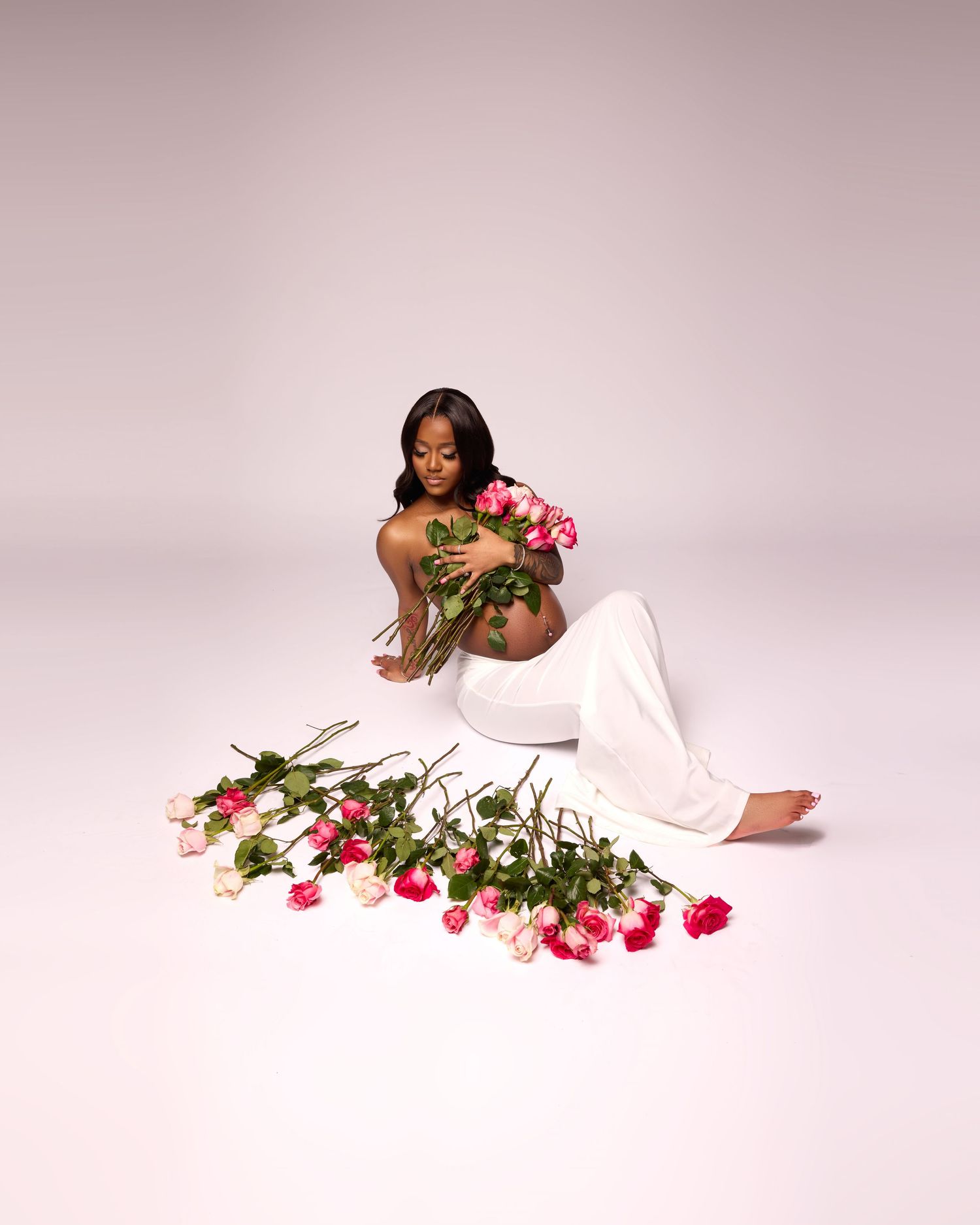 Artistic maternity photo with woman in white dress posed with scattered pink roses.