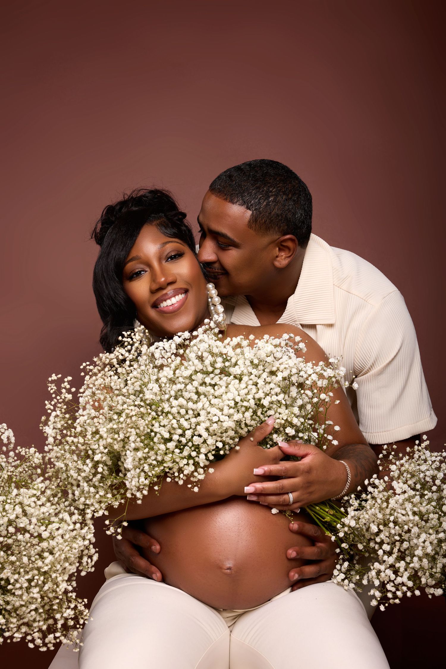 Tender maternity photos featuring baby's breath flowers and natural poses against warm brown backdrop.