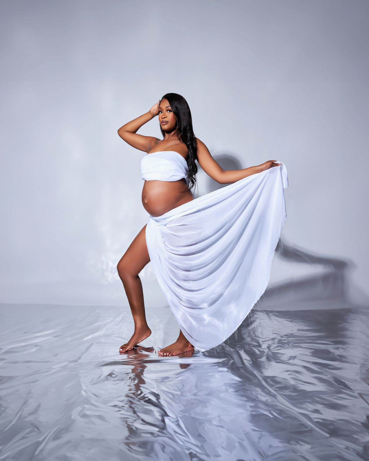 Dramatic maternity photo with flowing white fabric against reflective water surface.