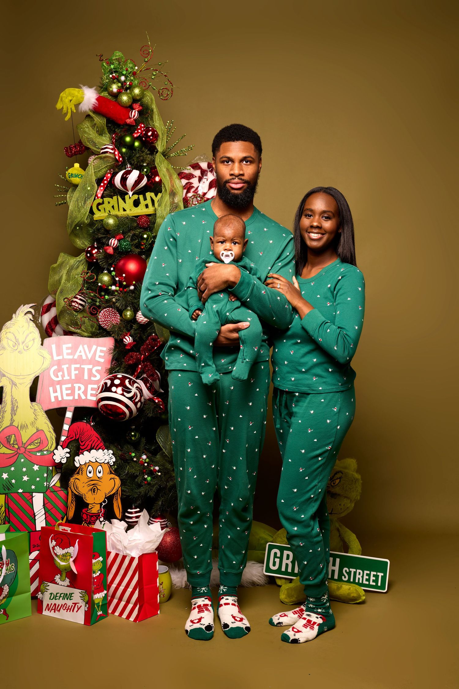 Family wearing matching green holiday pajamas poses by Christmas tree with festive decorations.