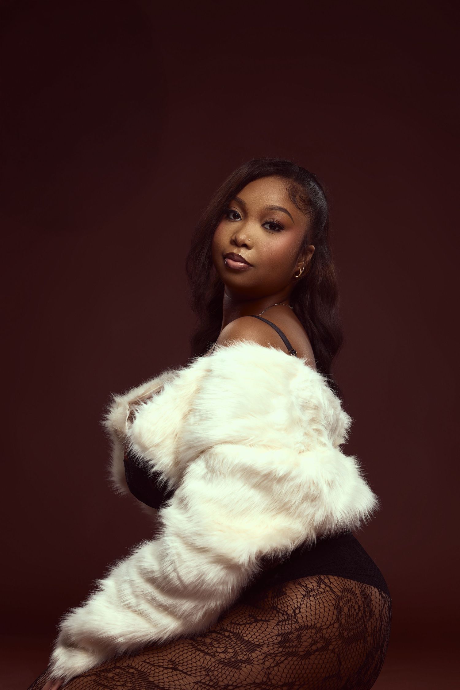 Glamour portrait featuring white fur coat against deep brown studio backdrop.