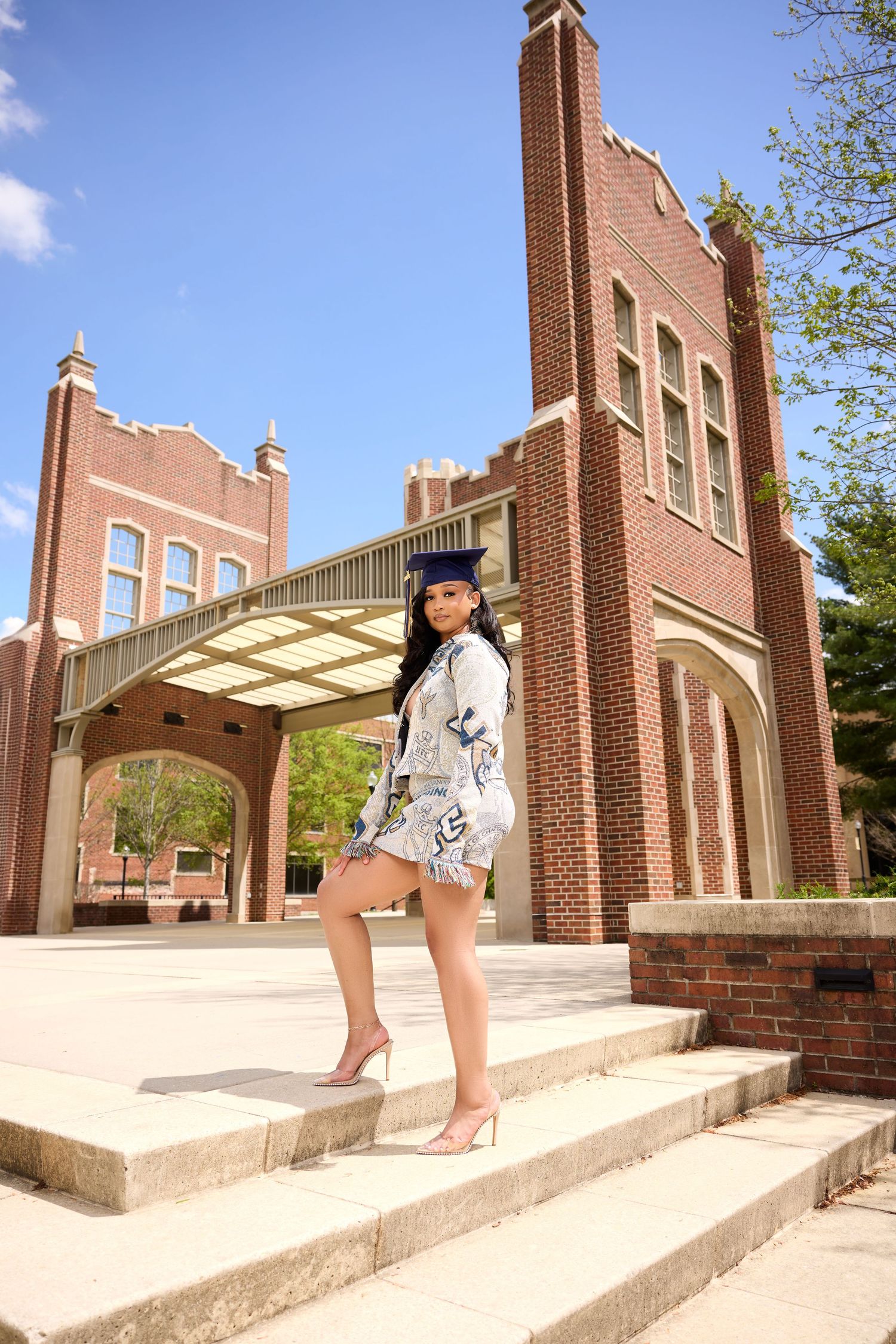 Graduate descends stone steps with brick academic building architecture in background.