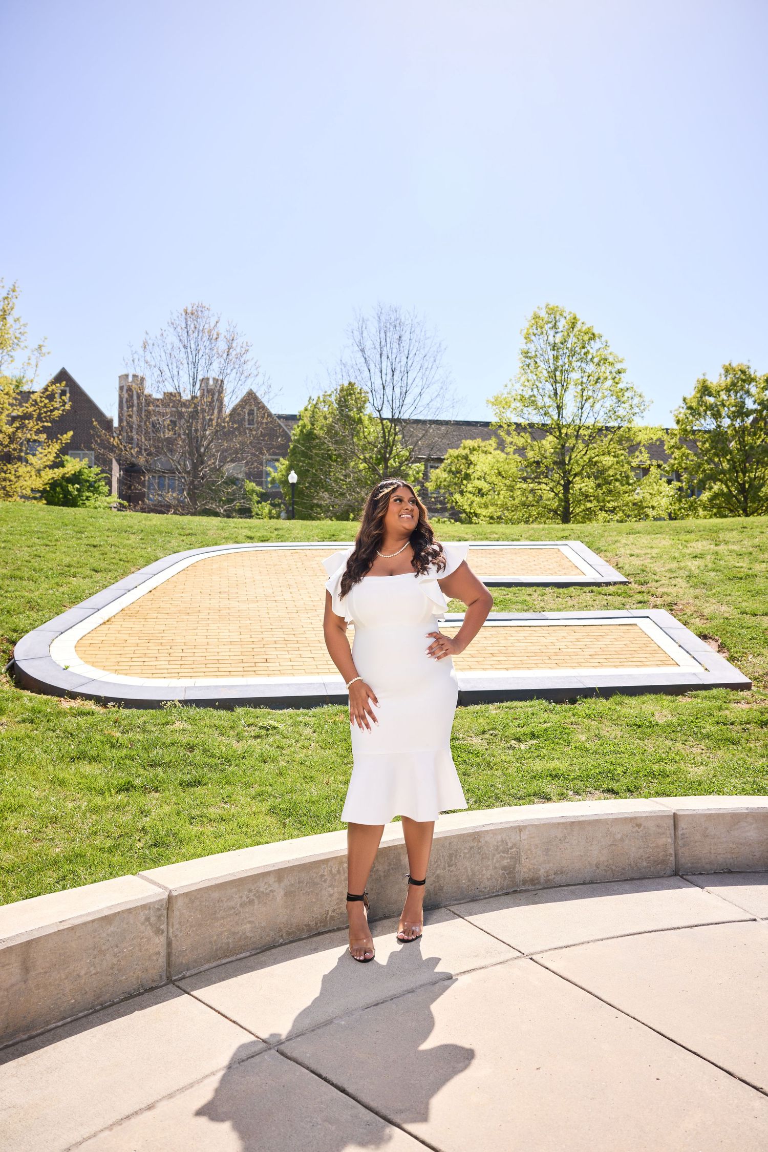 Graduate in white dress strikes poses on outdoor campus steps during photo session.