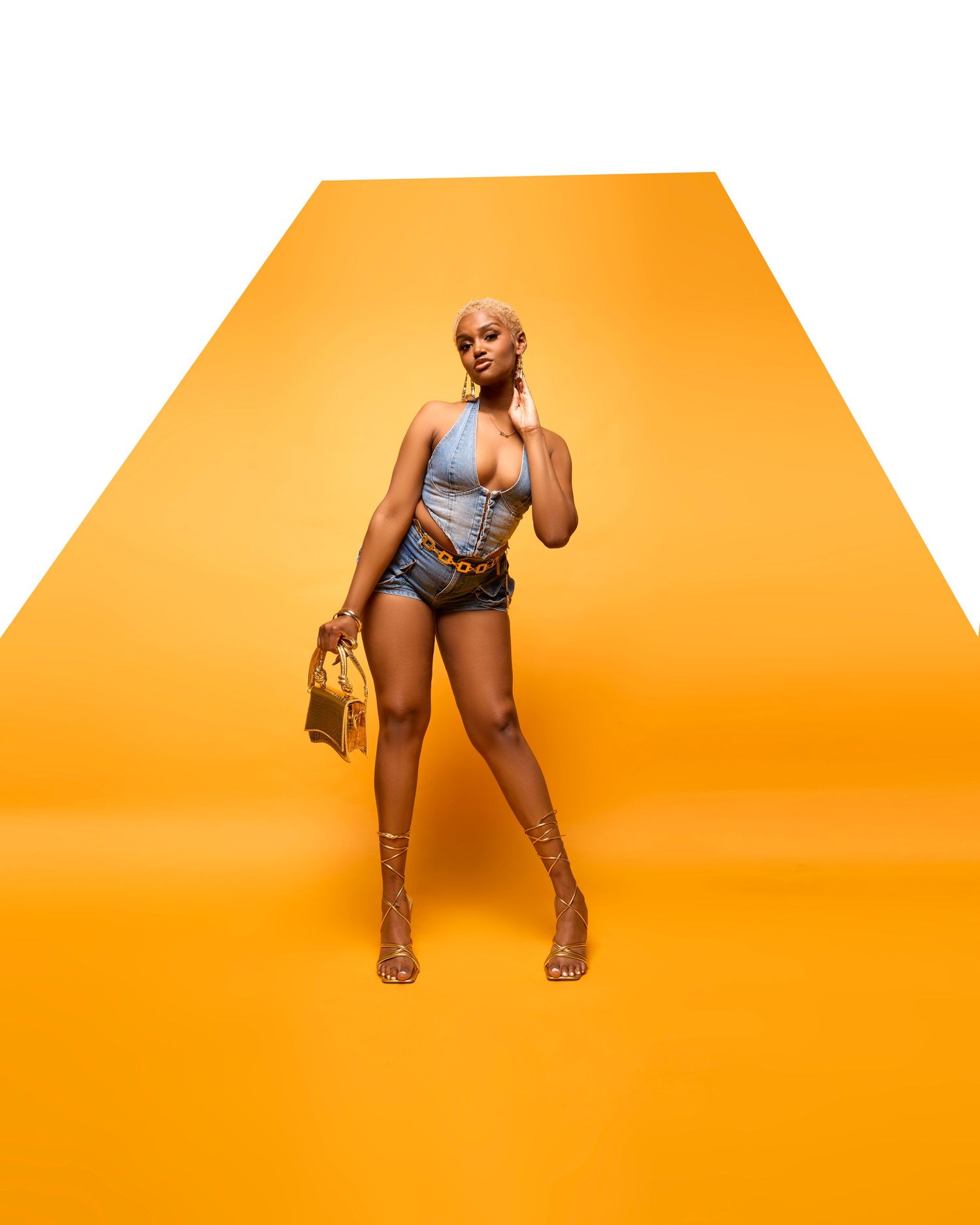Person in a silver bodysuit poses against a vibrant orange background in a dynamic fashion photoshoot series.