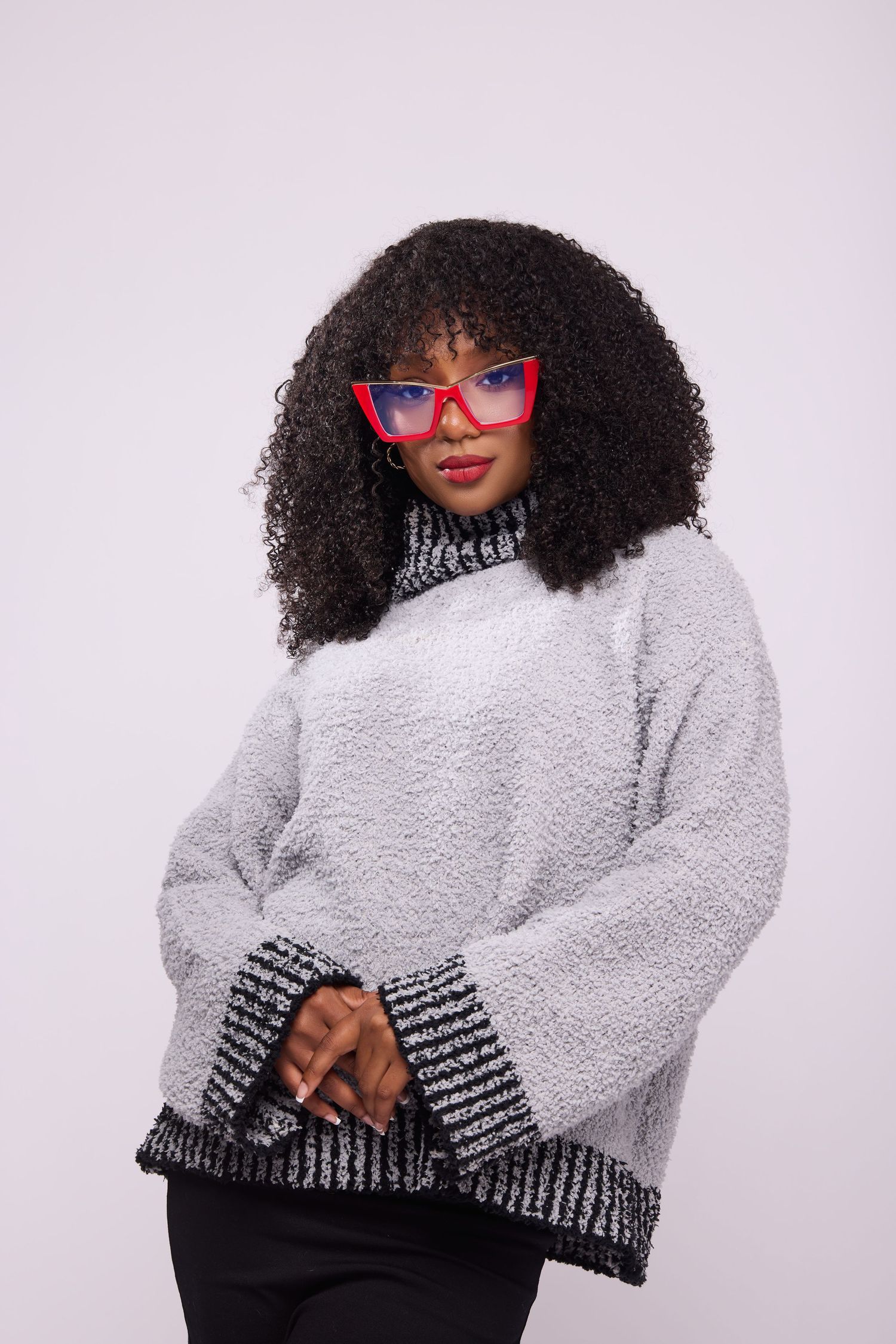 Model in fluffy gray sweater and red sunglasses poses against light background.