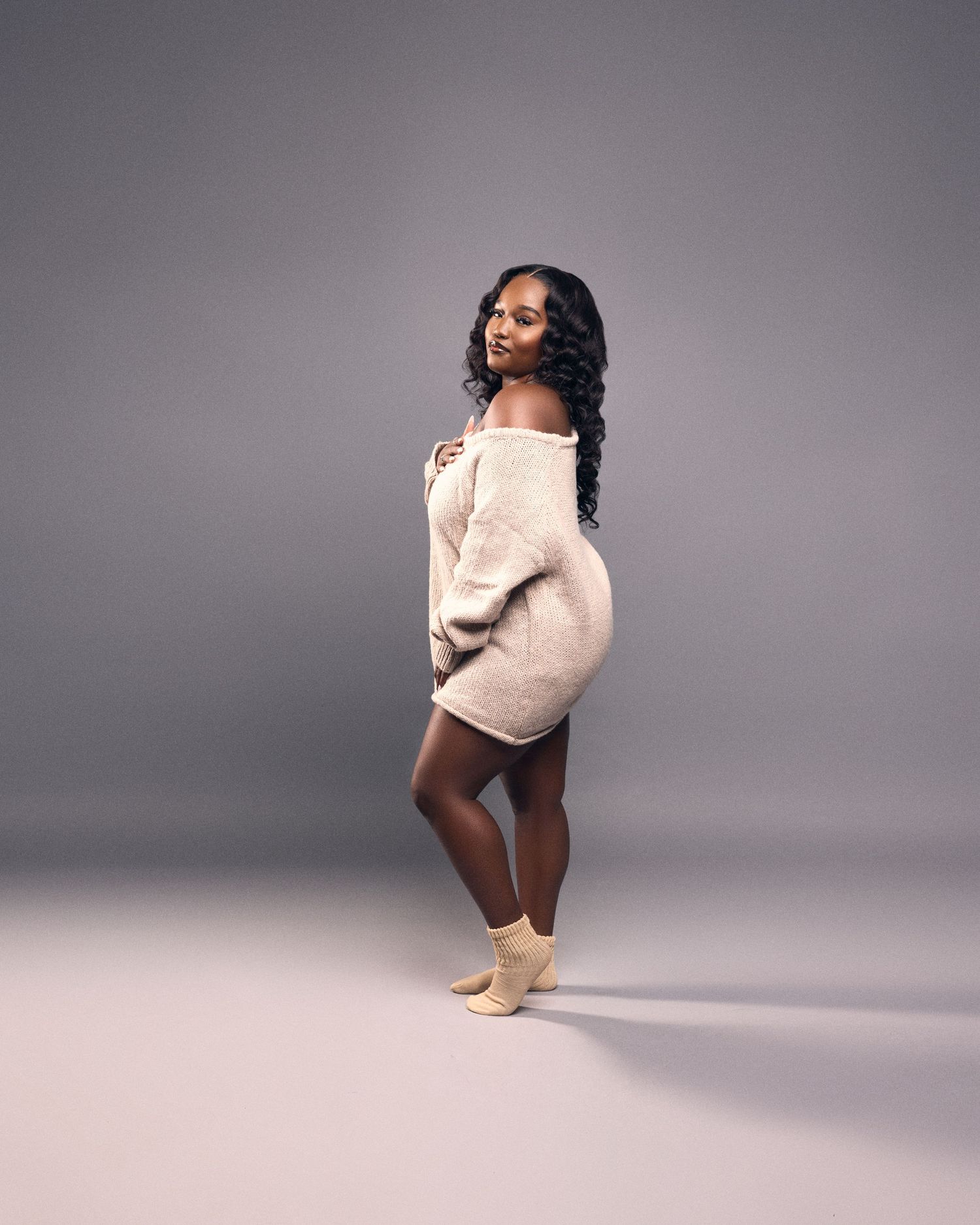 A figure in a pink sweater and brown shorts strikes dynamic dance poses against a gray studio backdrop.