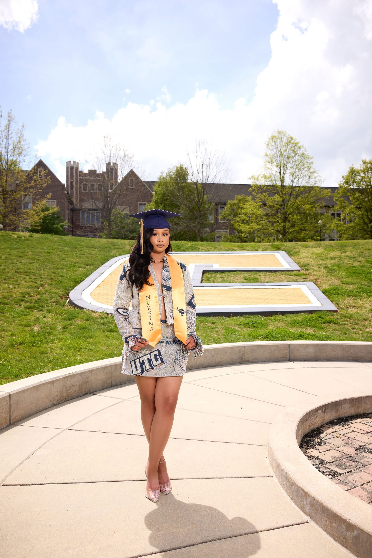Graduate in decorated cap and academic regalia poses on curved concrete walkway.