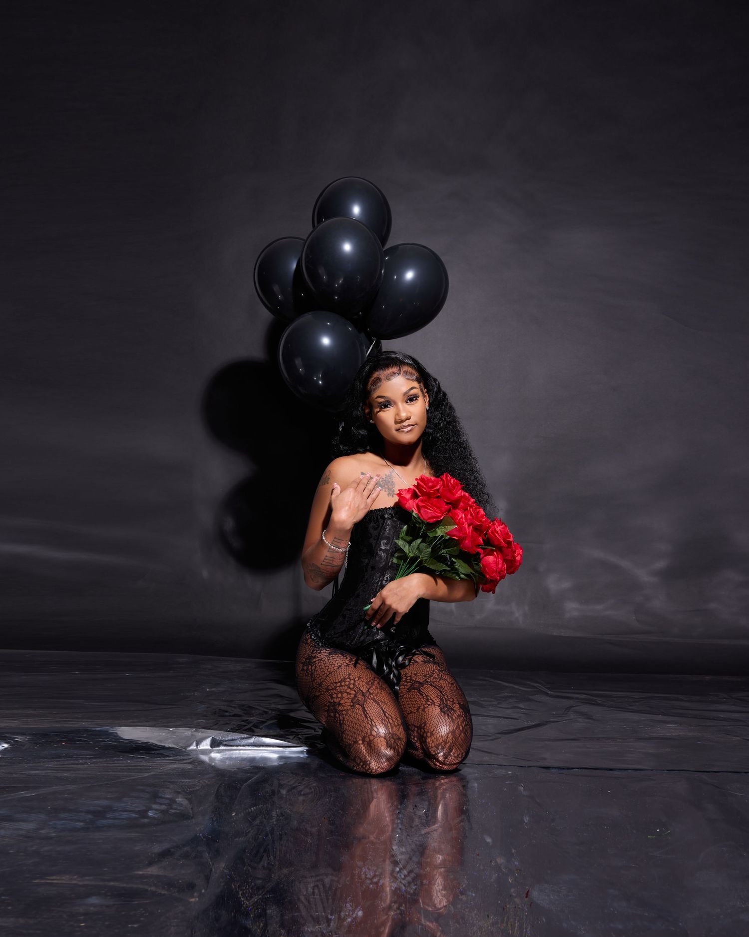 Artistic portrait with black balloons and red flowers on wet reflective surface.