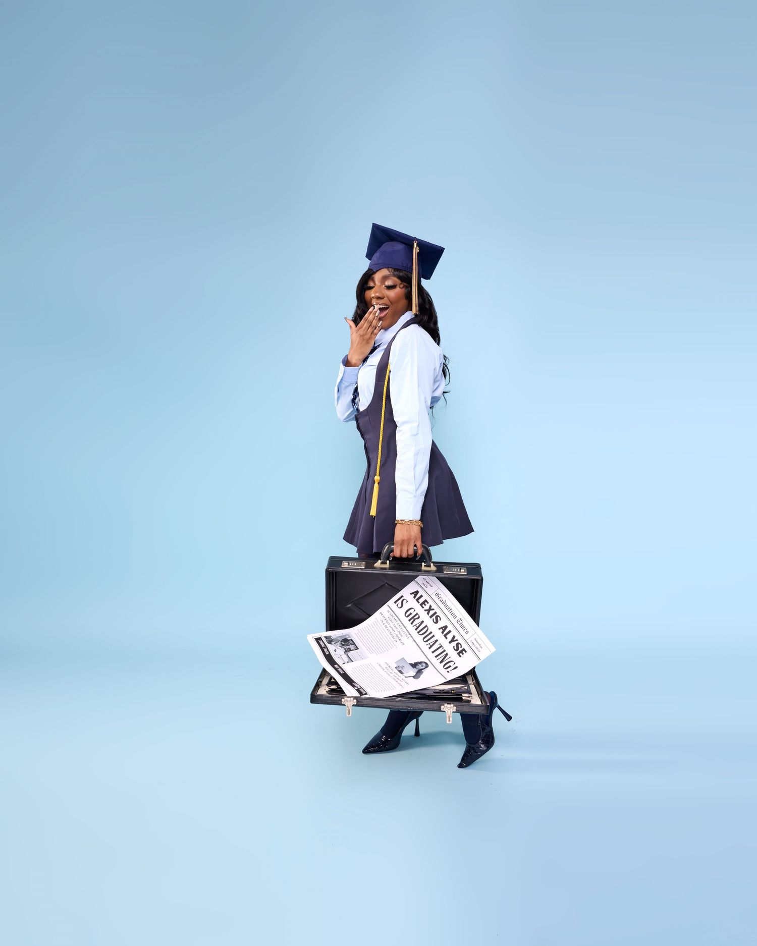 Graduate in academic regalia poses with diploma against light blue background.