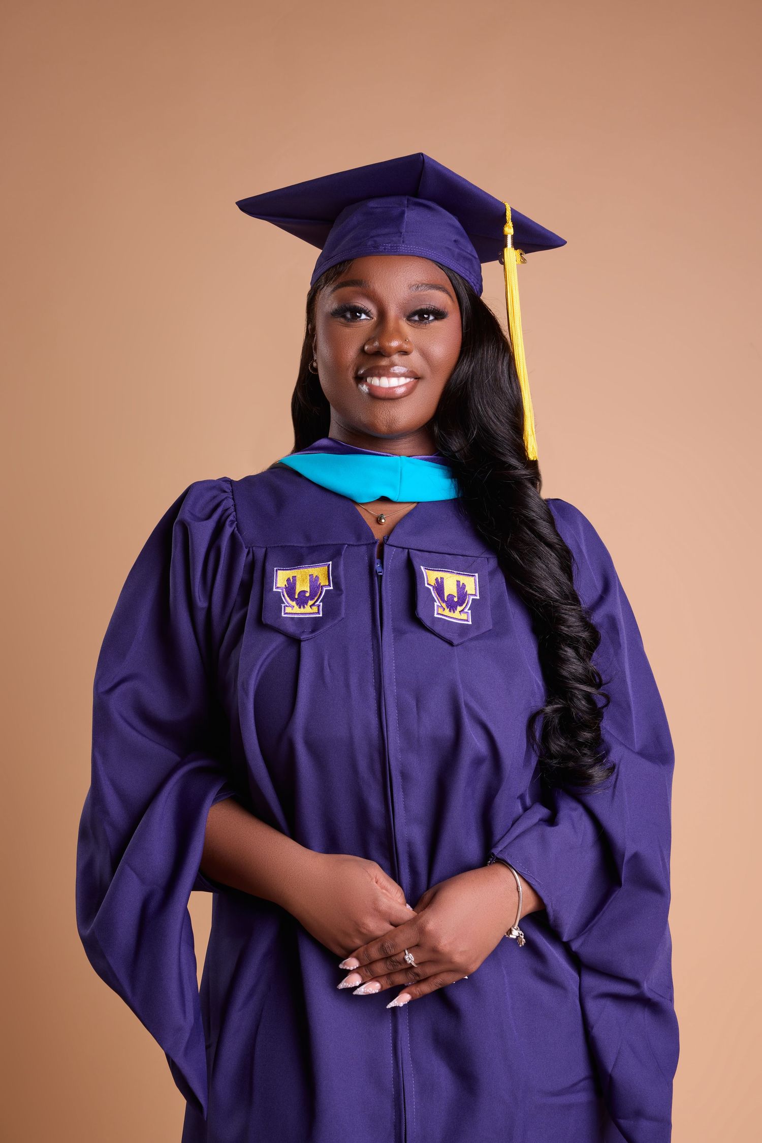 Young woman smiling in purple graduation cap and gown with gold tassel, posing for a professional portrait.
