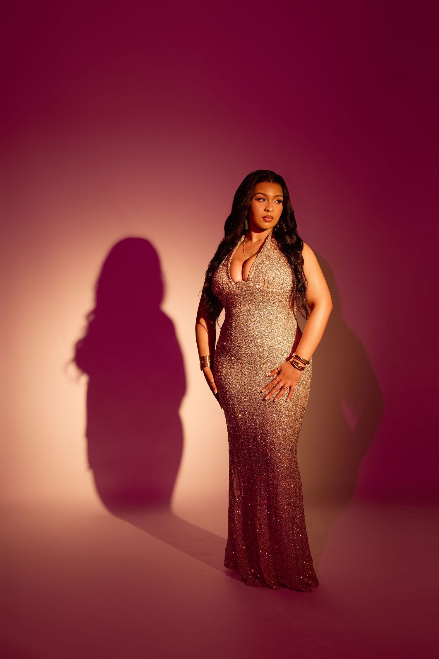 Dramatic silhouette poses in sequined gown against deep burgundy studio lighting.