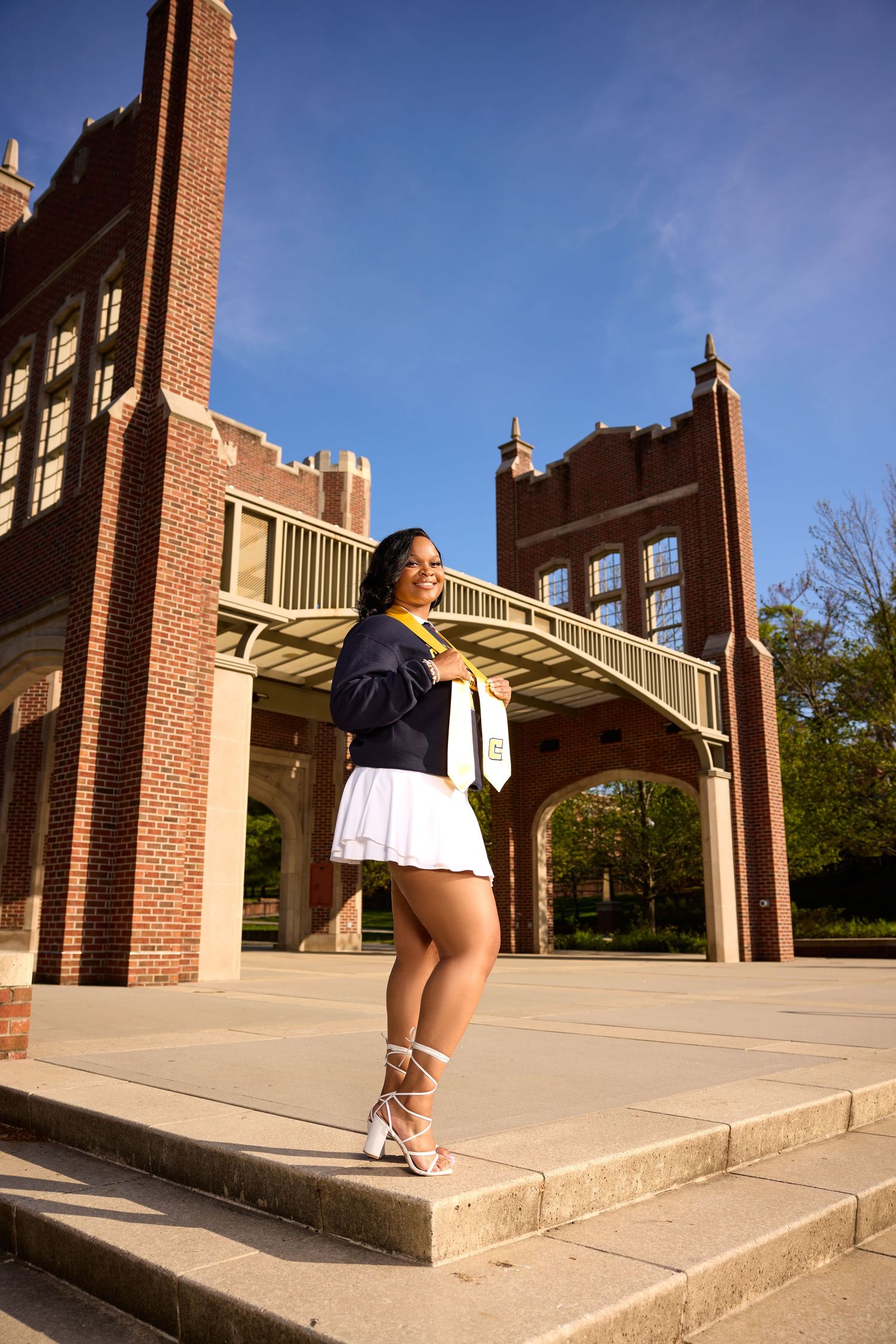Graduate poses on concrete steps with Gothic-style university architecture in background.